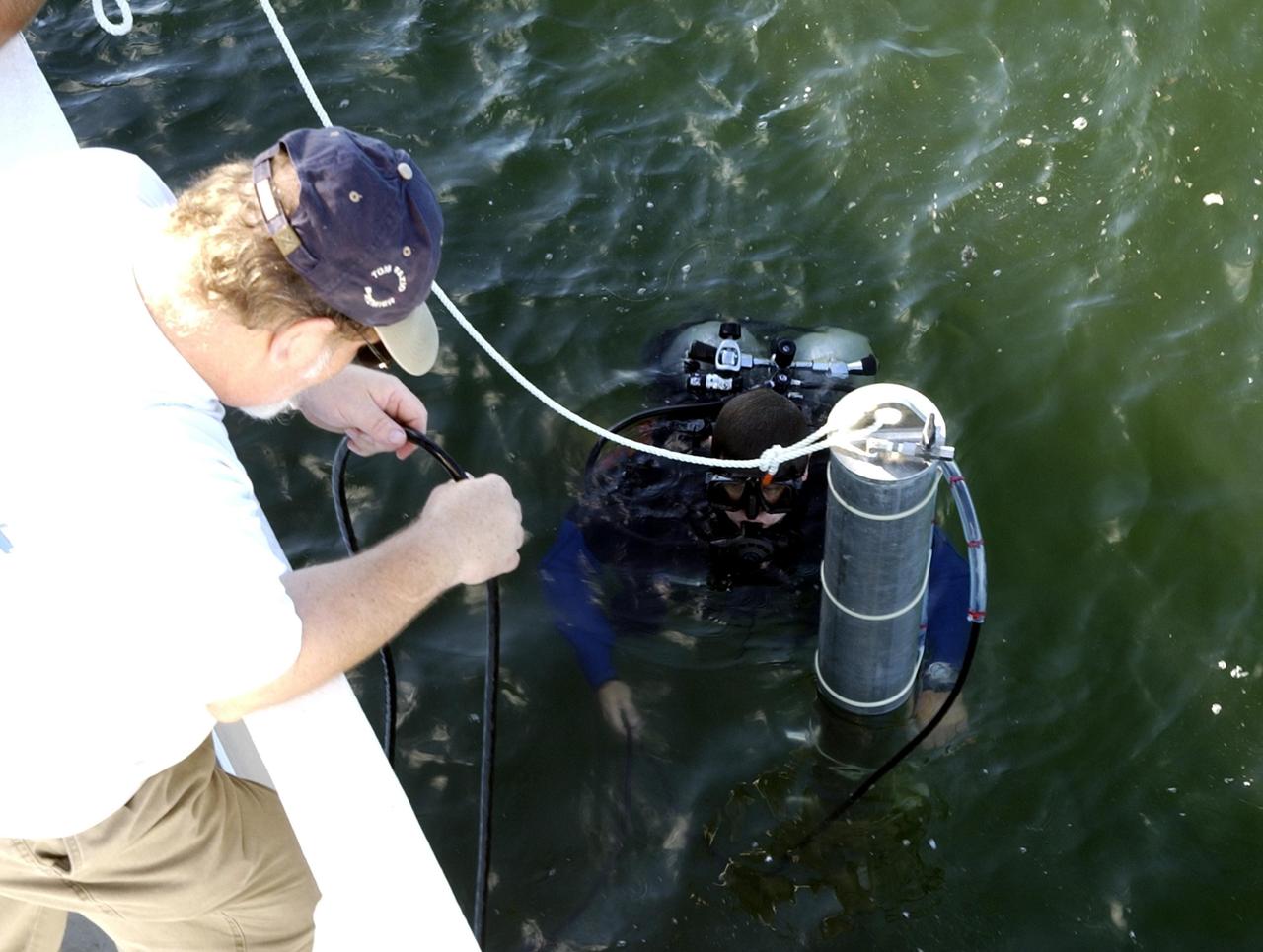 KENNEDY SPACE CENTER, FLA. -- A diver helps lower sonar mapping equipment into the water alongside the Liberty Star, one of NASA's solid rocket booster retrieval ships. The equipment will be attached to the ship's hull for an eight-day expedition surveying deep-water coral reefs on the Oculina Banks off eastern Florida.  NASA joins the National Oceanic and Atmospheric Administration (NOAA) and other ocean scientists for the sophisticated mapping system that will provide the first high-resolution, three-dimensional map of the Oculina Banks.  The survey results are expected to guide another expedition in Spring 2003, using NASA's ship, when the reef fish spawn.  Also used will be NASA's underwater robot and an acoustic hydrophone system for listening to fish and vessel noise.  Dive sites will be chosen based on the new charts.