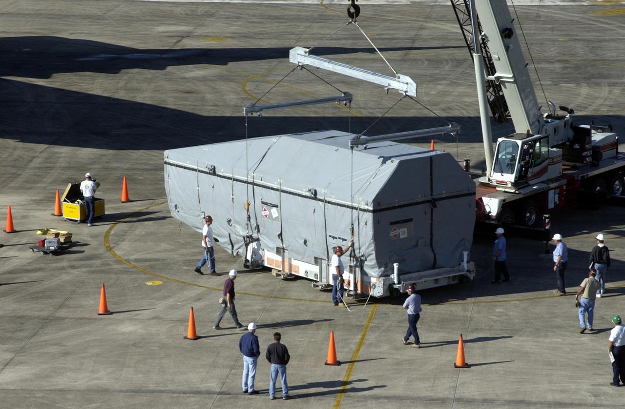 KENNEDY SPACE CENTER, FLA. -   Workers attach the container with the TDRS-J spacecraft inside to an overhead crane.  The container will be placed on a transporter and taken to the Spacecraft Assembly and Encapsulation Facility-2 (SAEF-2). TDRS-J is the third in the current series of three Tracking and Data Relay Satellites designed to replenish the existing on-orbit fleet of six spacecraft, the first of which was launched in 1983. The Tracking and Data Relay Satellite System is the primary source of space-to-ground voice, data and telemetry for the Space Shuttle. It also provides communications with the International Space Station and scientific spacecraft in low-earth orbit such as the Hubble Space Telescope, and launch support for some expendable vehicles. This new advanced series of satellites will extend the availability of TDRS communications services until approximately 2017.  
