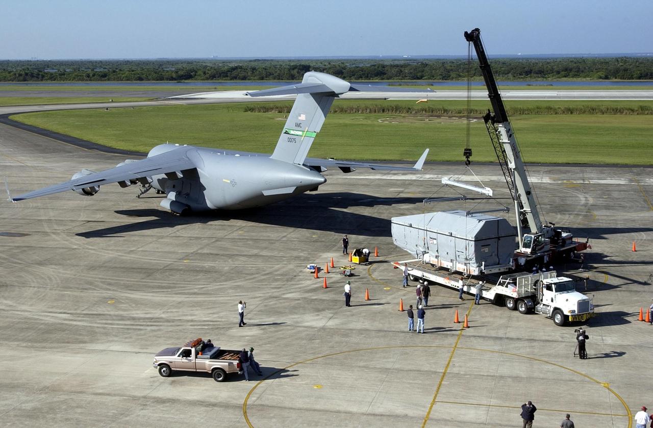 KENNEDY SPACE CENTER, FLA. - At the KSC Shuttle Landing Facility, an overhead crane lifts the container with the TDRS-J spacecraft onto a transport vehicle. In the background is the Air Force C-17 air cargo plane that delivered it. TDRS-J is the third in the current series of three Tracking and Data Relay Satellites designed to replenish the existing on-orbit fleet of six spacecraft, the first of which was launched in 1983. The Tracking and Data Relay Satellite System is the primary source of space-to-ground voice, data and telemetry for the Space Shuttle. It also provides communications with the International Space Station and scientific spacecraft in low-earth orbit such as the Hubble Space Telescope, and launch support for some expendable vehicles. This new advanced series of satellites will extend the availability of TDRS communications services until approximately 2017.