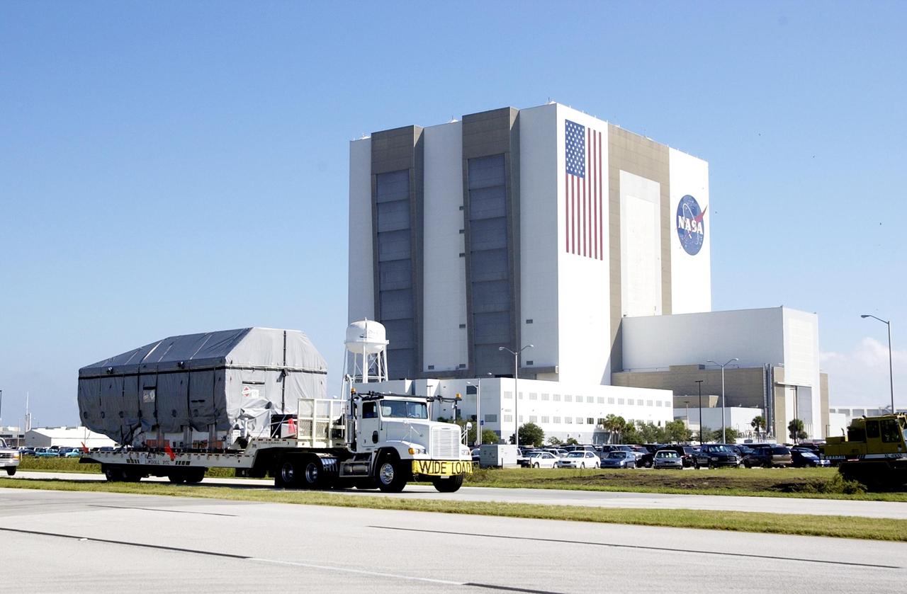 KENNEDY SPACE CENTER, FLA. -  The TDRS-J spacecraft, enclosed in a container, is transported  past the Vehicle Assembly Building on its way to the Spacecraft Assembly and Encapsulation Facility-2 (SAEF-2) for processing. The Tracking and Data Relay Satellite System is the primary source of space-to-ground voice, data and telemetry for the Space Shuttle. It also provides communications with the International Space Station and scientific spacecraft in low-earth orbit such as the Hubble Space Telescope, and launch support for some expendable vehicles. This new advanced series of satellites will extend the availability of TDRS communications services until approximately 2017.