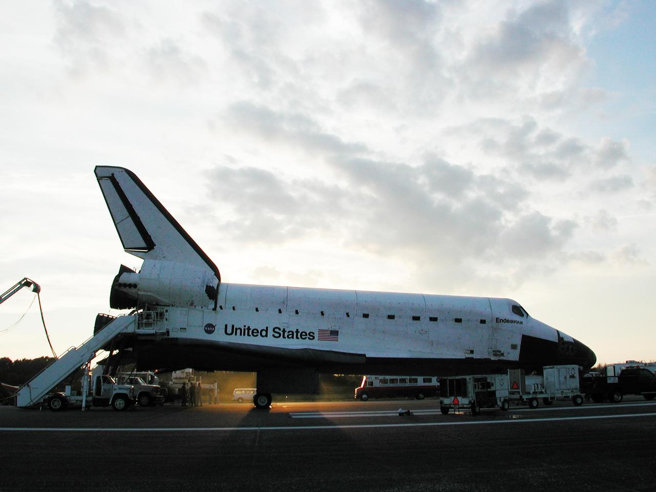 KENNEDY SPACE CENTER, FLA. -  Space Shuttle Endeavour is surrounded by vehicles from the landing convoy, as the sun sets on runway 33 at the Shuttle Landing Facility at the conclusion of the 13-day, 18-hour, 48-minute, 5.74-million mile STS-113 mission to the International Space Station. Under the orbiter, the Convoy Command Vehicle, the command post for the Convoy Commander, can be seen on the far side of the runway.  The Convoy Commander is in communication with the orbiter and all of the landing convoy vehicles during the post-landing operations.  The landing convoy's purpose is to safe the vehicle and provide support for the disembarking crew and experiments.  Main gear touchdown was at 2:37:12 p.m. EST, nose gear touchdown was at 2:37:23 p.m., and wheel stop was at 2:38:25 p.m. Poor weather conditions thwarted landing opportunities until a fourth day, the first time in Shuttle program history that a landing has been waved off for three consecutive days. The vehicle carries the STS-113 crew, Commander James Wetherbee, Pilot Paul Lockhart and Mission Specialists Michael Lopez-Alegria and John Herrington, as well as the returning Expedition Five crew, Commander Valeri Korzun, ISS Science Officer Peggy Whitson and Flight Engineer Sergei Treschev. The installation of the P1 truss on the International Space Station was accomplished during the mission.