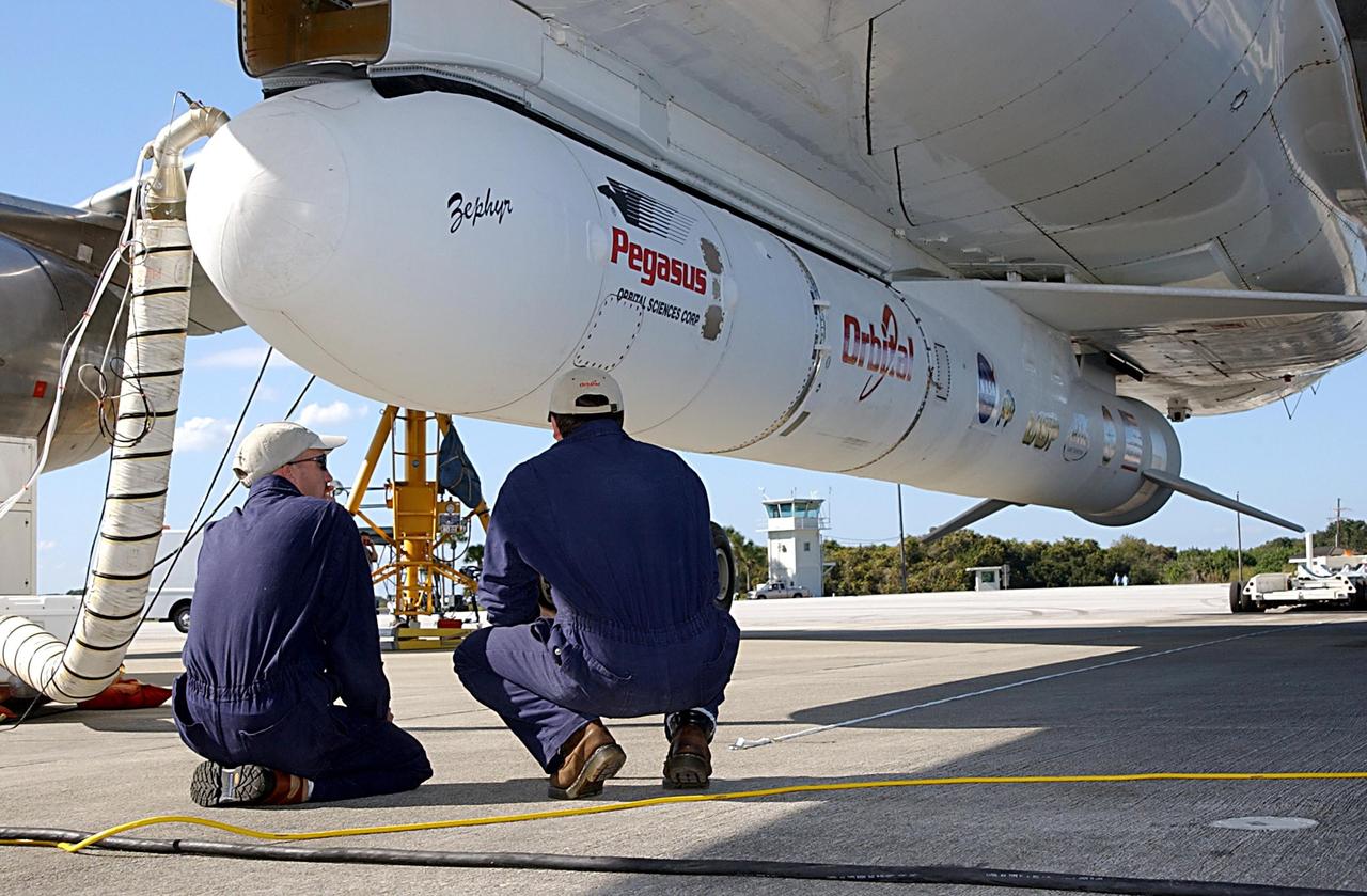 KENNEDY SPACE CENTER, FLA. -- Workers oversee the repositioning of a transporter below a Pegasus XL Expendable Launch Vehicle before its detachment from the underside of an Orbital Sciences L-1011 aircraft. The aircraft, with the launch vehicle nestled beneath, arrived at the Cape Canaveral Air Force Station Skid Strip on Dec. 17. The Pegasus XL will undergo three flight simulations prior to its scheduled launch in late January 2003. It will carry NASA's Solar Radiation and Climate Experiment (SORCE) spacecraft into orbit. Built by Orbital Sciences Space Systems Group, SORCE will study and measure solar irradiance as a source of energy in the Earth's atmosphere with instruments built by the University of Colorado's Laboratory for Atmospheric and Space Physics (LASP).