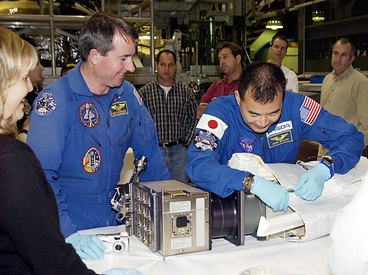 KENNEDY SPACE CENTER, FLA. -- STS-114 Mission Specialist Soichi Noguchi (right), with the National Space Development Agency of Japan (NASDA), works with equipment as Mission Specialist Stephen K. Robinson, Ph.D., (left) watches. The STS-114 crew is participating in familiarization activities with the hardware that will fly on the mission. STS-114 is a utilization and logistics flight (ULF-1) that will carry Multi-Purpose Logistics Module Raffaello and the External Stowage Platform (ESP-2), as well as the Expedition 7 crew, to the International Space Station. Launch is targeted for March 1, 2003.