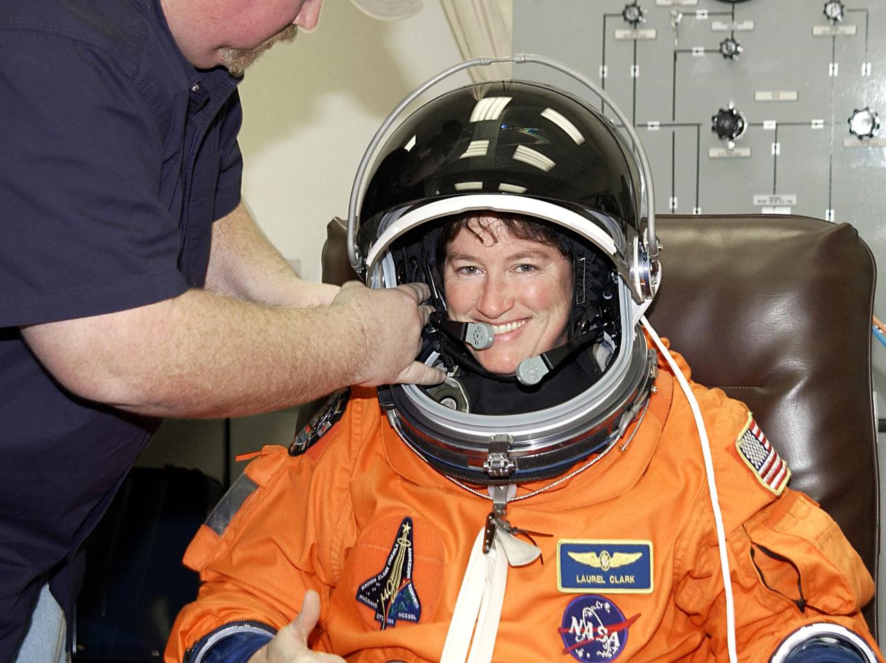 KENNEDY SPACE CENTER, FLA. - STS-107 Mission Specialist Laurel Clark is helped with her helmet during suitup for launch. STS-107 is a mission devoted to research and will include more than 80 experiments that will study Earth and space science, advanced technology development, and astronaut health and safety. The payload on Space Shuttle Columbia includes FREESTAR (Fast Reaction Experiments Enabling Science, Technology, Applications and Research) and the SHI Research Double Module (SHI/RDM), known as SPACEHAB.  Experiments on the module range from material sciences to life sciences.  Liftoff is scheduled for 10:39 a.m. EST.