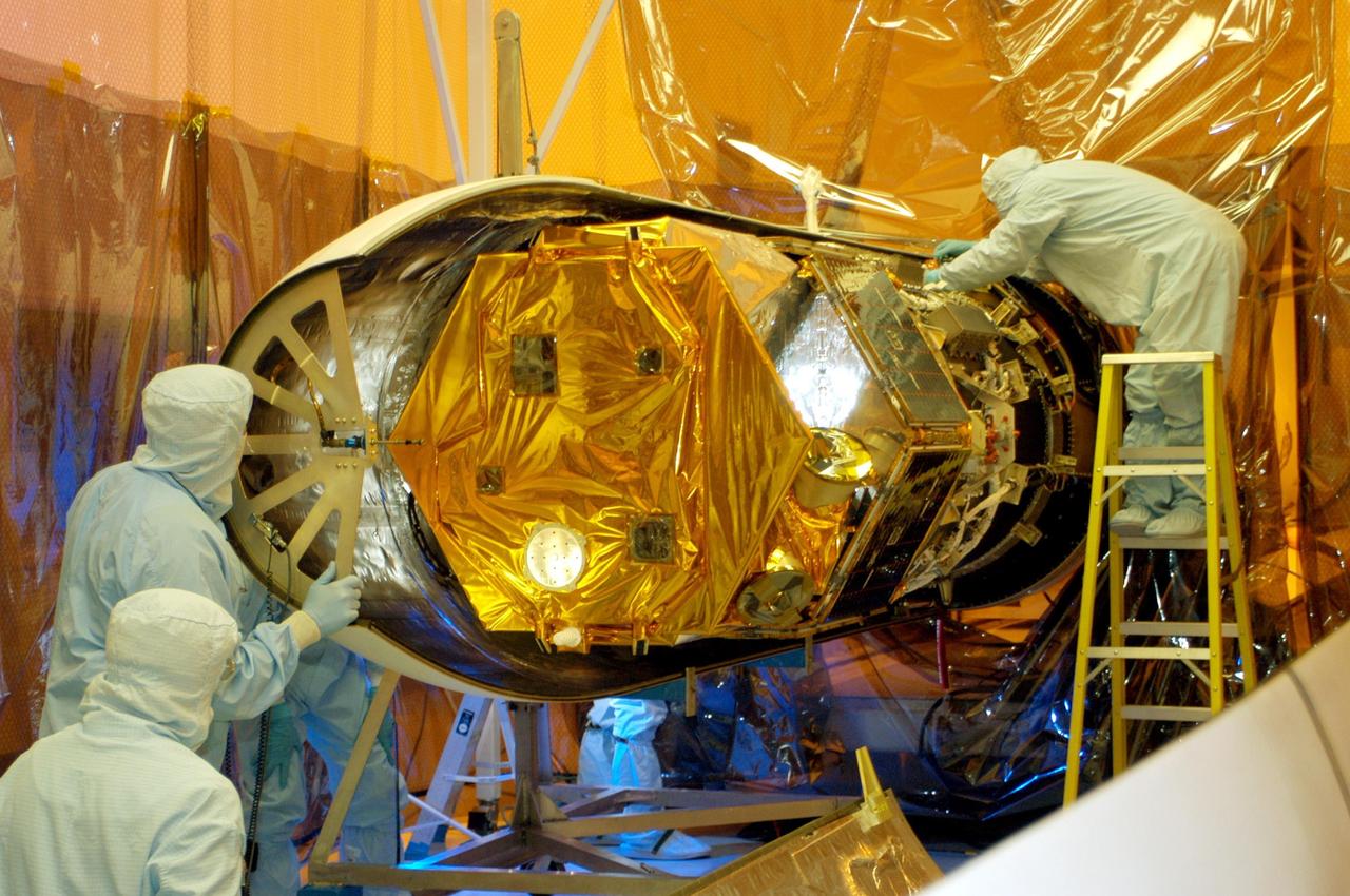 KENNEDY SPACE CENTER, FLA. -- Workers in the Multi-Purpose Processing Facility look over the Solar Radiation and Climate Experiment (SORCE) satellite after the first half of the fairing is put in place. When completely encapsulated, the satellite will be installed in the Pegasus XL launch vehicle. Built by Orbital Sciences Corporation (OSC), SORCE will study and measure solar irradiance as a source of energy in the Earth's atmosphere. The launch of SORCE is scheduled for Jan. 25 at 3:14 p.m. from Cape Canaveral Air Force Station, Fla. The drop of the Pegasus will be from OSC's L-1011 aircraft at an altitude of 39,000 feet over the Atlantic Ocean approximately 100 miles east-southeast of Cape Canaveral.