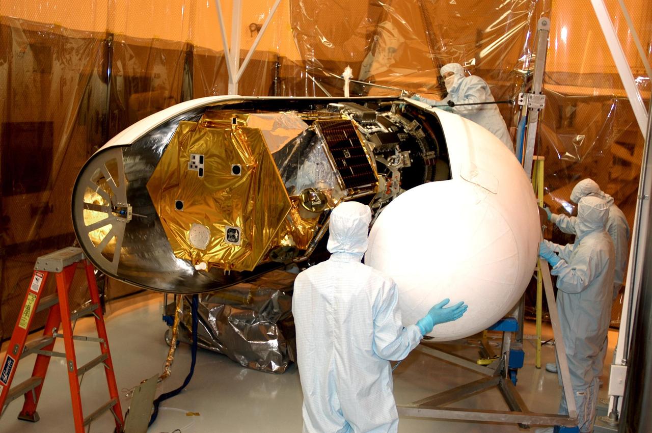 KENNEDY SPACE CENTER, FLA. -- Workers in the Multi-Purpose Processing Facility move the second half of the fairing into place around the Solar Radiation and Climate Experiment (SORCE) satellite (left). When complete, the satellite will be installed in the Pegasus XL launch vehicle. Built by Orbital Sciences Corporation (OSC), SORCE will study and measure solar irradiance as a source of energy in the Earth's atmosphere. The launch of SORCE is scheduled for Jan. 25 at 3:14 p.m. from Cape Canaveral Air Force Station, Fla. The drop of the Pegasus will be from OSC's L-1011 aircraft at an altitude of 39,000 feet over the Atlantic Ocean approximately 100 miles east-southeast of Cape Canaveral.