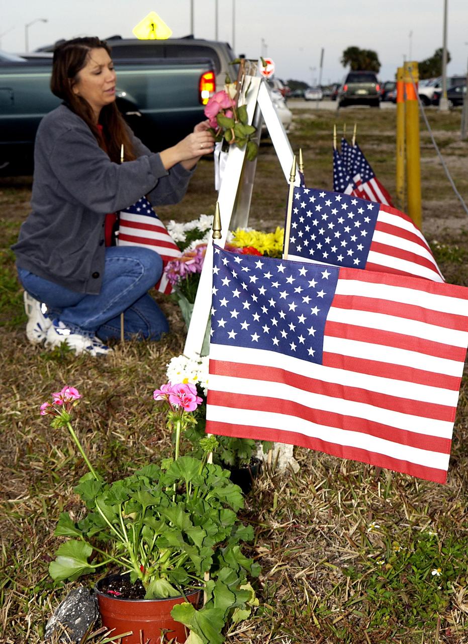 KENNEDY SPACE CENTER, FLA. - At the corner of Contractors Road and the Saturn Causeway, a KSC employee places an STS-107 crew photograph and surrounds it with flowers and U.S. flags as a memorial tribute to the fallen crew of Columbia. The Space Shuttle Columbia and her crew of seven were lost on Feb. 1, 2003, over East Texas as they returned to Earth after a 16-day research mission, STS-107.