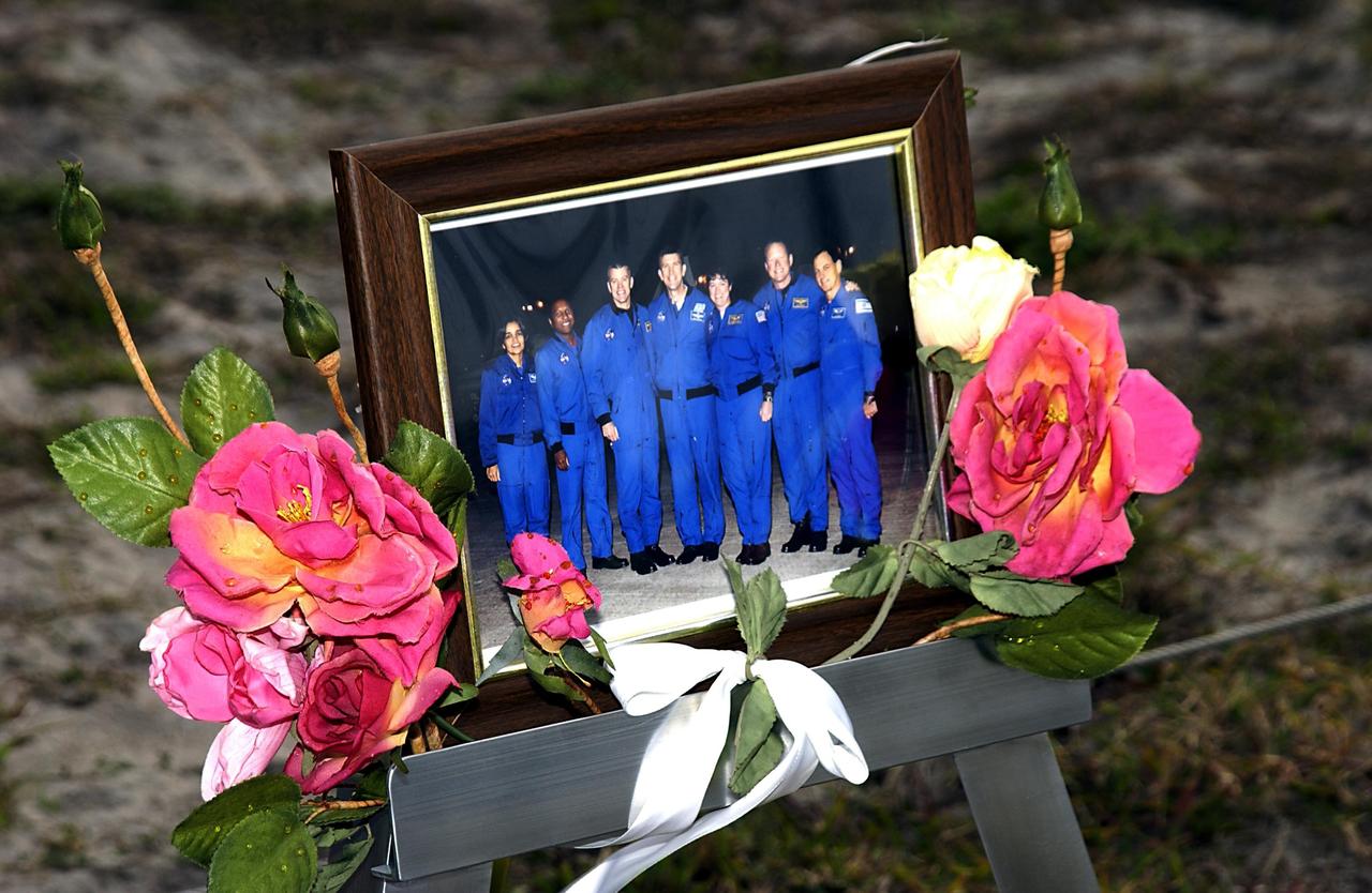 KENNEDY SPACE CENTER, FLA. - At the corner of Contractors Road and the Saturn Causeway, an STS-107 crew photograph, surrounded with flowers and U.S. flags, stands as a memorial tribute to the fallen crew of Columbia by KSC employees. The Space Shuttle Columbia and her crew of seven were lost on Feb. 1, 2003, over East Texas as they returned to Earth after a 16-day research mission, STS-107.