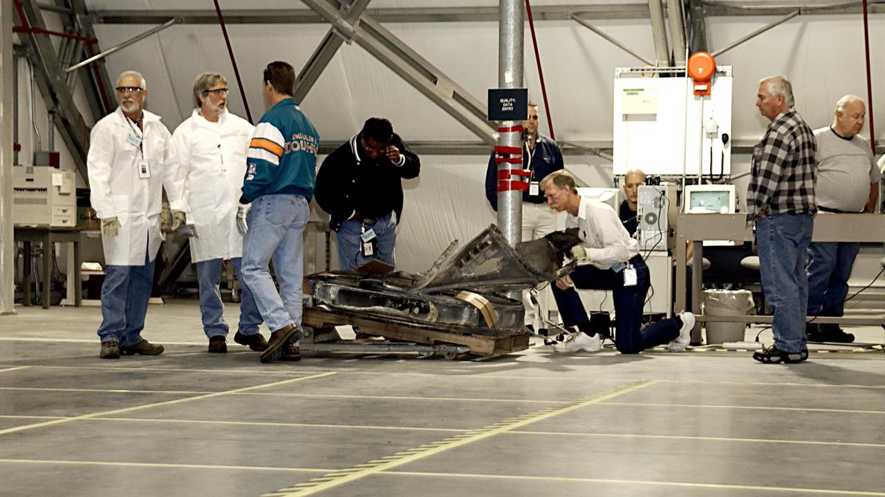 KENNEDY SPACE CENTER, FLA. - Workers inside the RLV Hangar near the Shuttle Landing Facility look at a piece of the Columbia debris newly arrived from the collection point at Barksdale Air Force Base, Shreveport, La. The workers will attempt to reconstruct the orbiter as part of the ongoing investigation of the accident that destroyed the Columbia and claimed the lives of seven astronauts as they returned to Earth after a 16-day research mission, STS-107. .