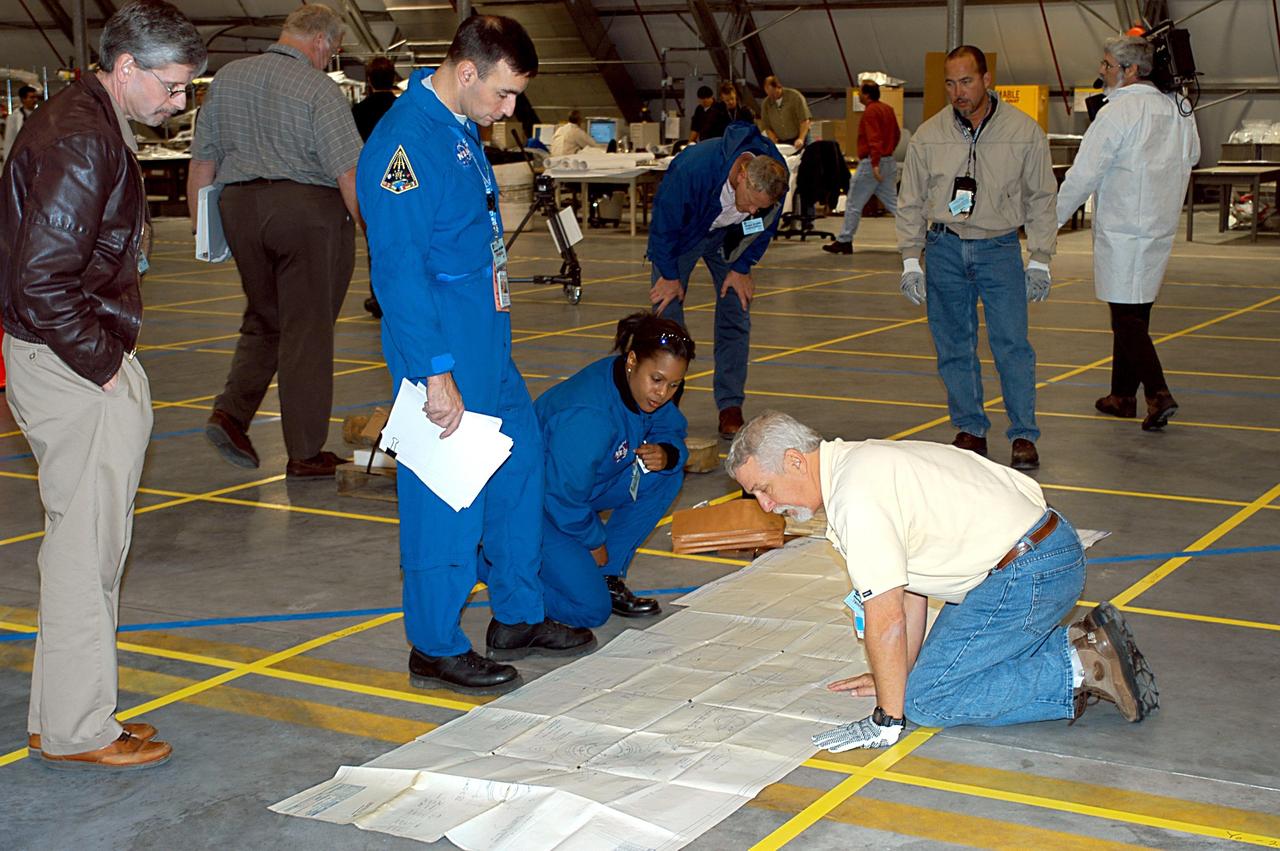 KENNEDY SPACE CENTER, FLA. -- Members of the Columbia reconstruction team look at a diagram on the floor of the RLV Hangar. In the background are pieces of the Columbia debris being examined and recorded. As part of the ongoing investigation into the tragic accident, workers will attempt to reconstruct the orbiter inside the RLV.