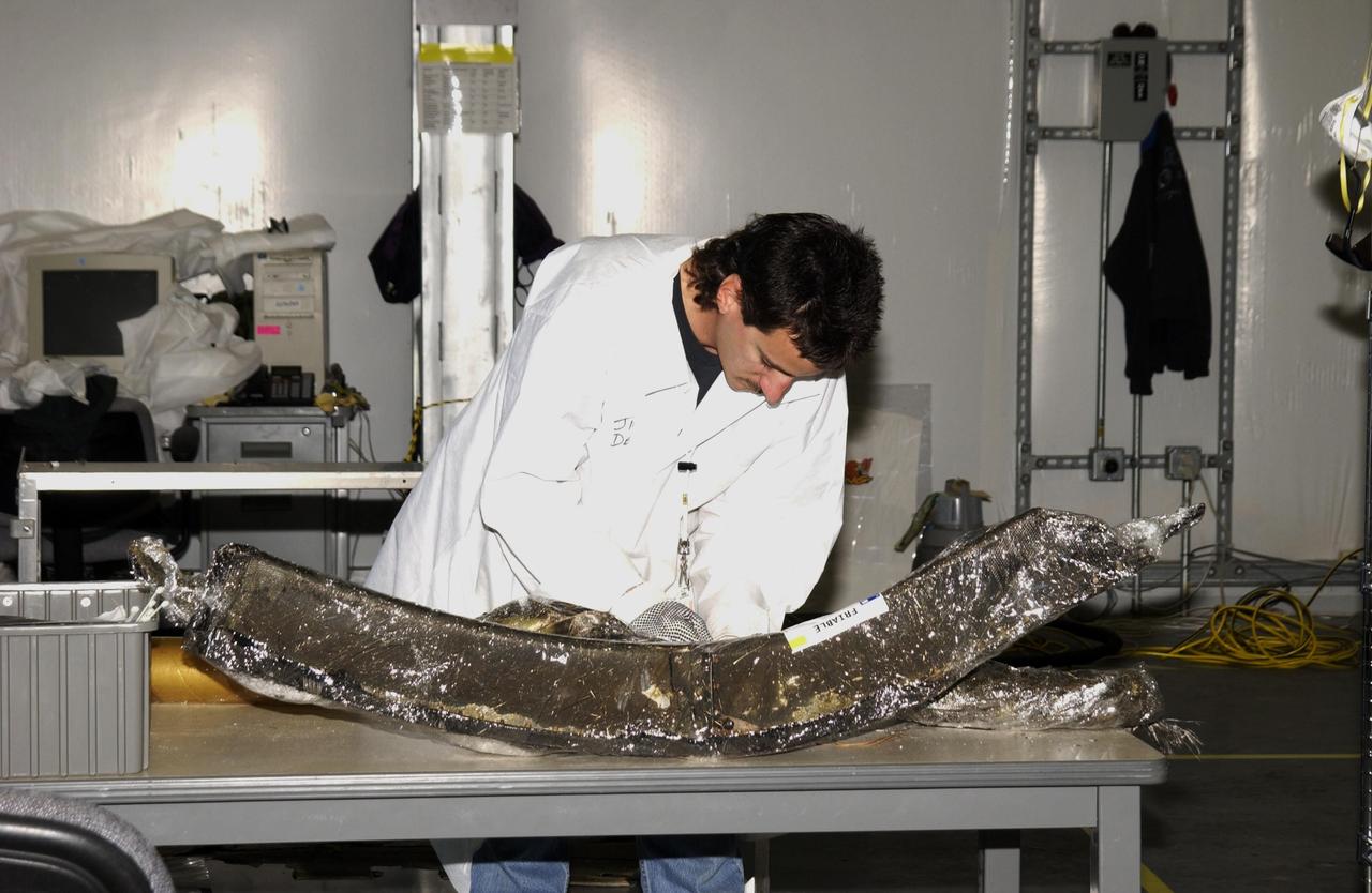 KENNEDY SPACE CENTER, FLA. -- A Columbia Reconstruction Project Team member examines debris from the Space Shuttle Columbia in the RLV Hangar.  The debris is being shipped to KSC from the collection point at Barksdale Air Force Base, Shreveport, La. As part of the ongoing investigation into the tragic accident that claimed Columbia and her crew of seven, workers will attempt to reconstruct the orbiter inside the hangar.