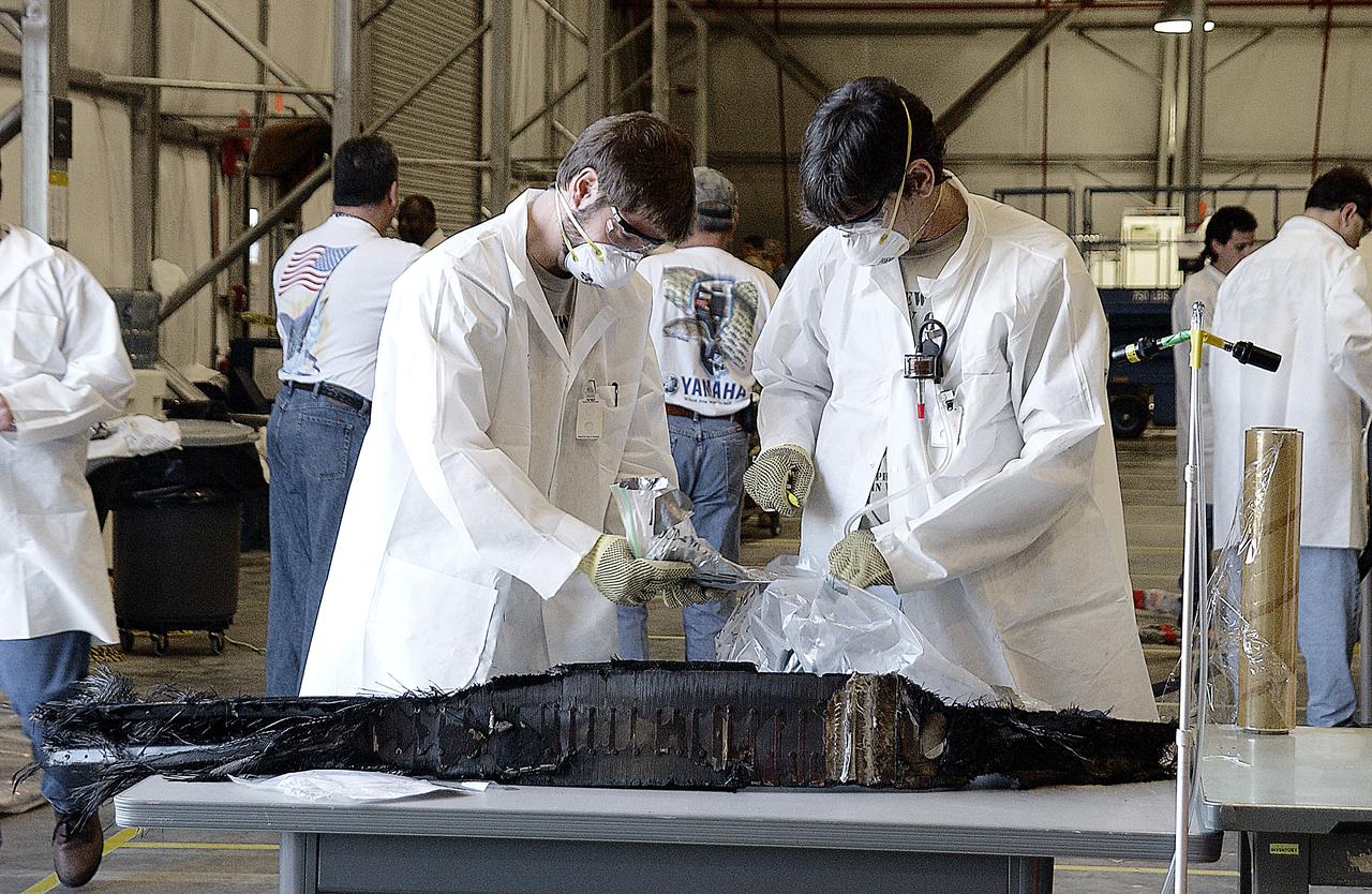 Columbia Reconstruction Project Team members cautiously examine potentially hazardous debris from the Space Shuttle Columbia in the RLV Hangar. The debris is being shipped to KSC from the collection point at Barksdale Air Force Base, Shreveport, La. As part of the ongoing investigation into the tragic accident that claimed Columbia and her crew of seven, workers will attempt to reconstruct the orbiter inside the hangar.                        