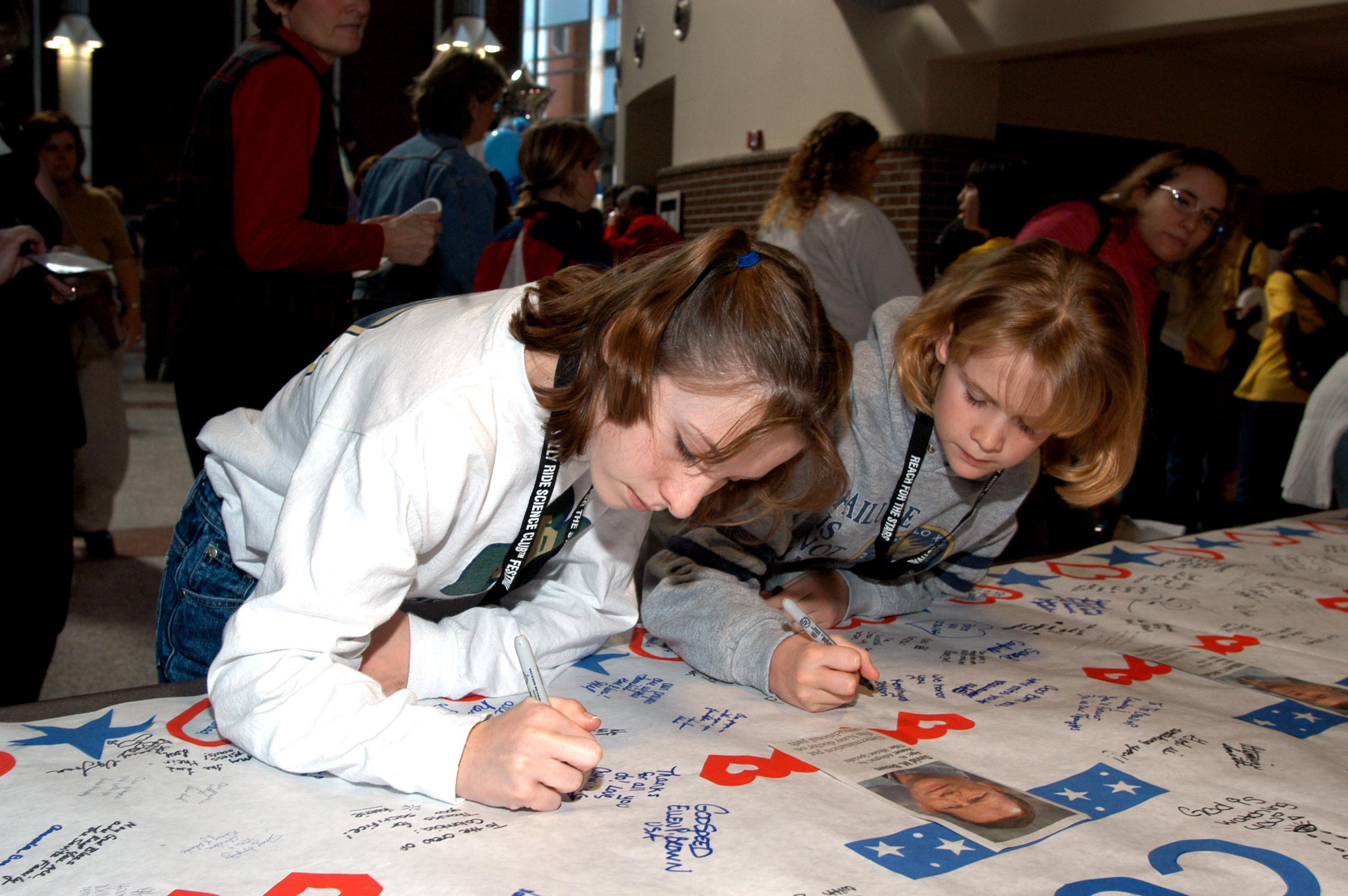 KENNEDY SPACE CENTER, FLA. -- At the Sally Ride Science Festival, held at the University of Central Florida, Orlando, Fla., young women gather to sign a large poster in tribute to the Columbia astronauts who were lost in the Shuttle's explosion the day before. The Sally Ride event promotes science, math and technology as future career paths for girls. Former astronaut Sally Ride addressed the girls, while breakout sessions afforded closer interaction between Ride and festival attendees.