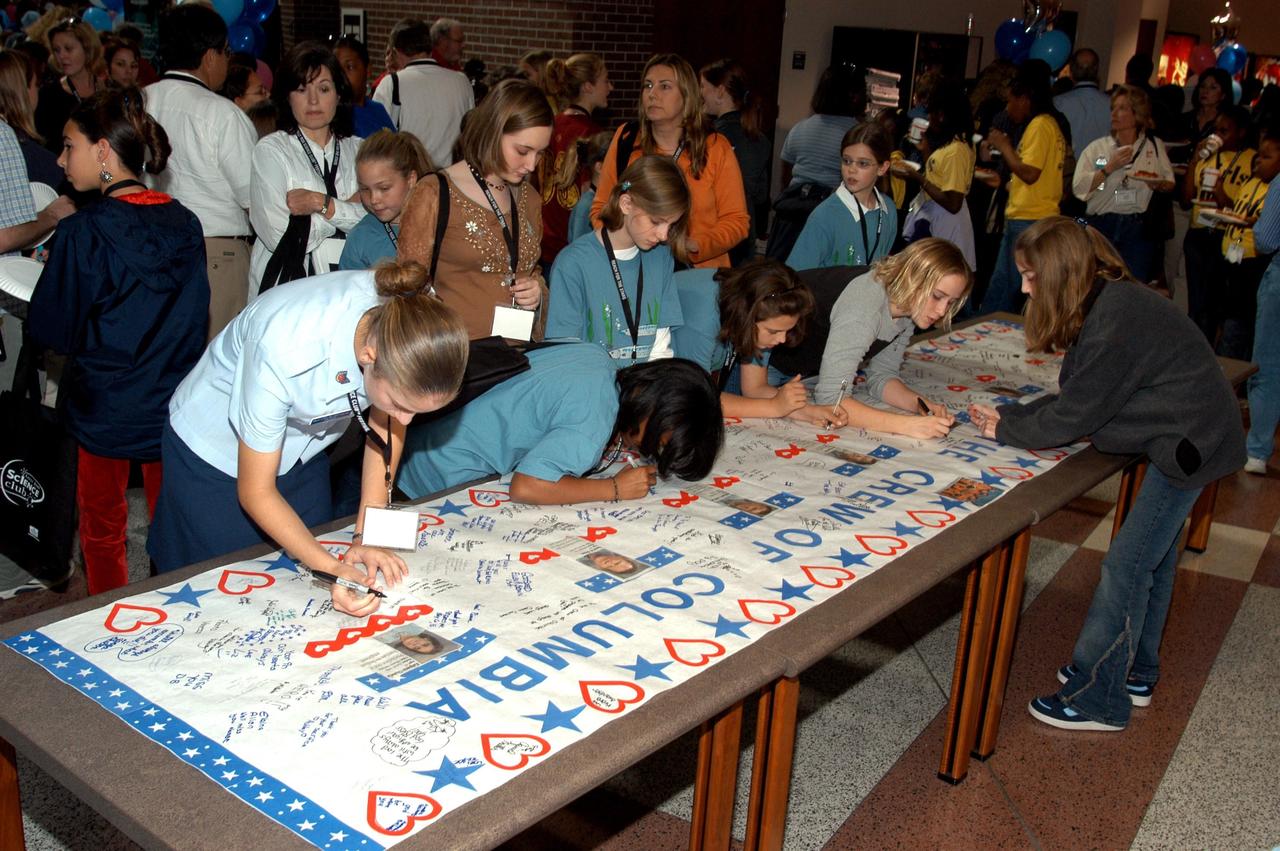 KENNEDY SPACE CENTER, FLA. -- At the Sally Ride Science Festival, held at the University of Central Florida, Orlando, Fla., young women gather to sign a large poster in tribute to the Columbia astronauts who were lost in the Shuttle's explosion the day before. The Sally Ride event promotes science, math and technology as future career paths for girls. Former astronaut Sally Ride addressed the girls, while breakout sessions afforded closer interaction between Ride and festival attendees.