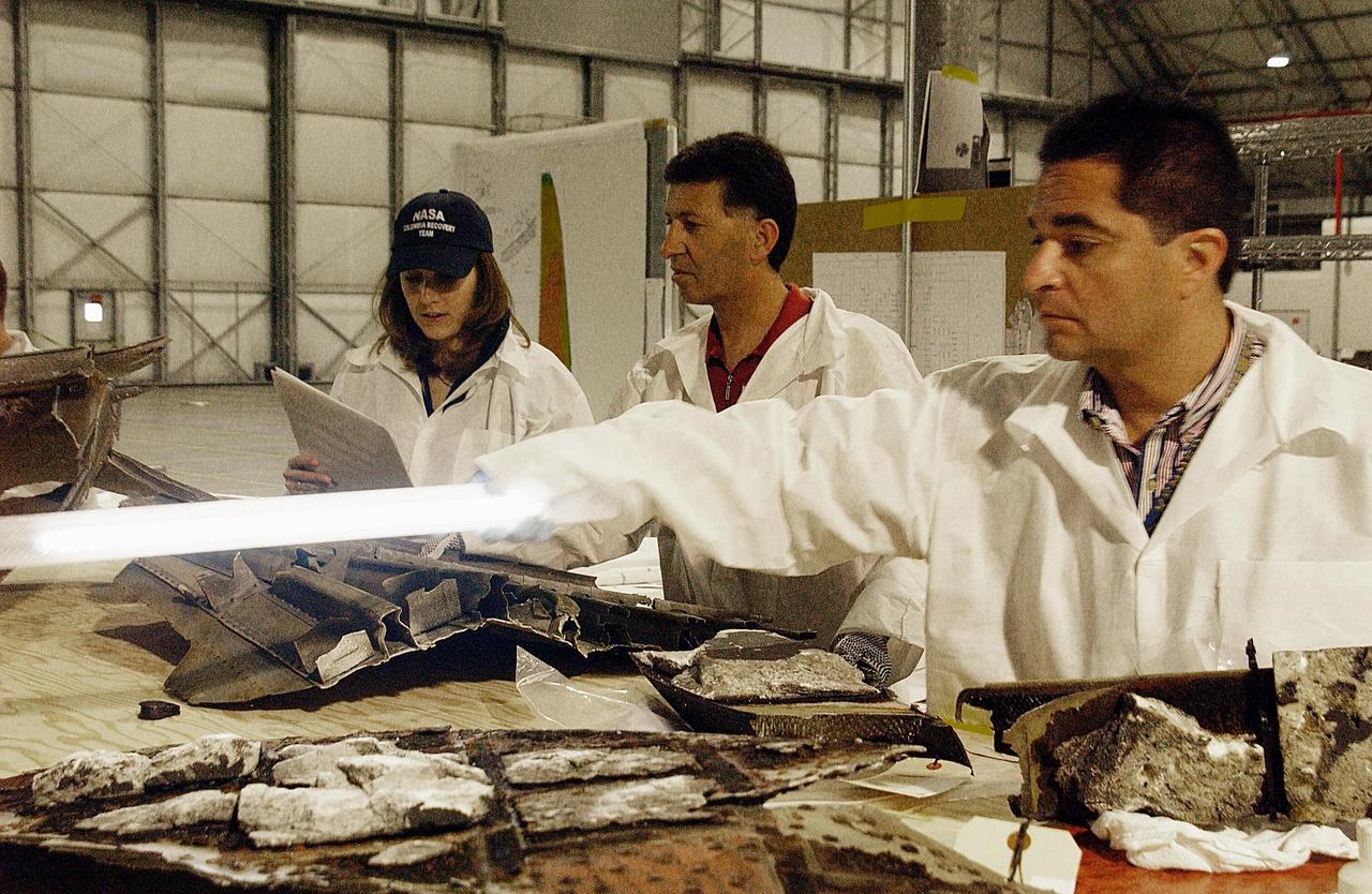 KENNEDY SPACE CENTER, FLA. --  -- Members of the Columbia Reconstruction Program Team pass a light over debris from Columbia. Workers are attempting to reconstruct the orbiter inside the hangar as part of the ongoing investigation into the tragic accident that claimed Columbia and her crew of seven returning from mission STS-107.