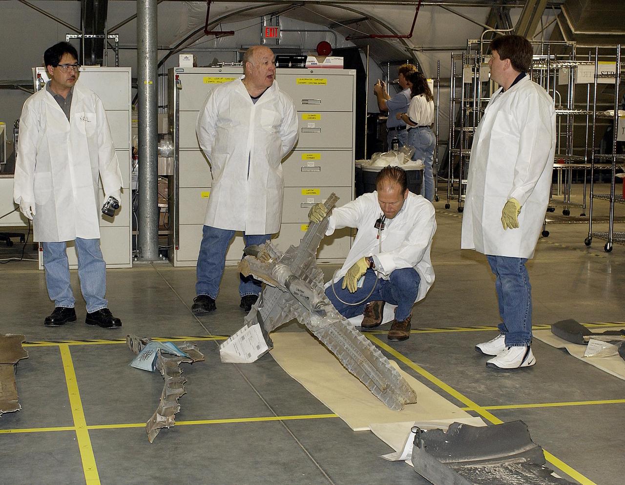 KENNEDY SPACE CENTER, FLA. - Members of the Columbia Restoration Project Team look at a piece of debris on the floor of the RLV Hangar at KSC. The team is examining pieces and attempting to reconstruct the orbiter as part of the investigation into the accident that caused the destruction of Columbia on its return to Earth from mission STS-107. To date, four shipments have arrived from Barksdale AFB, Shreveport, La., the collection point for debris.