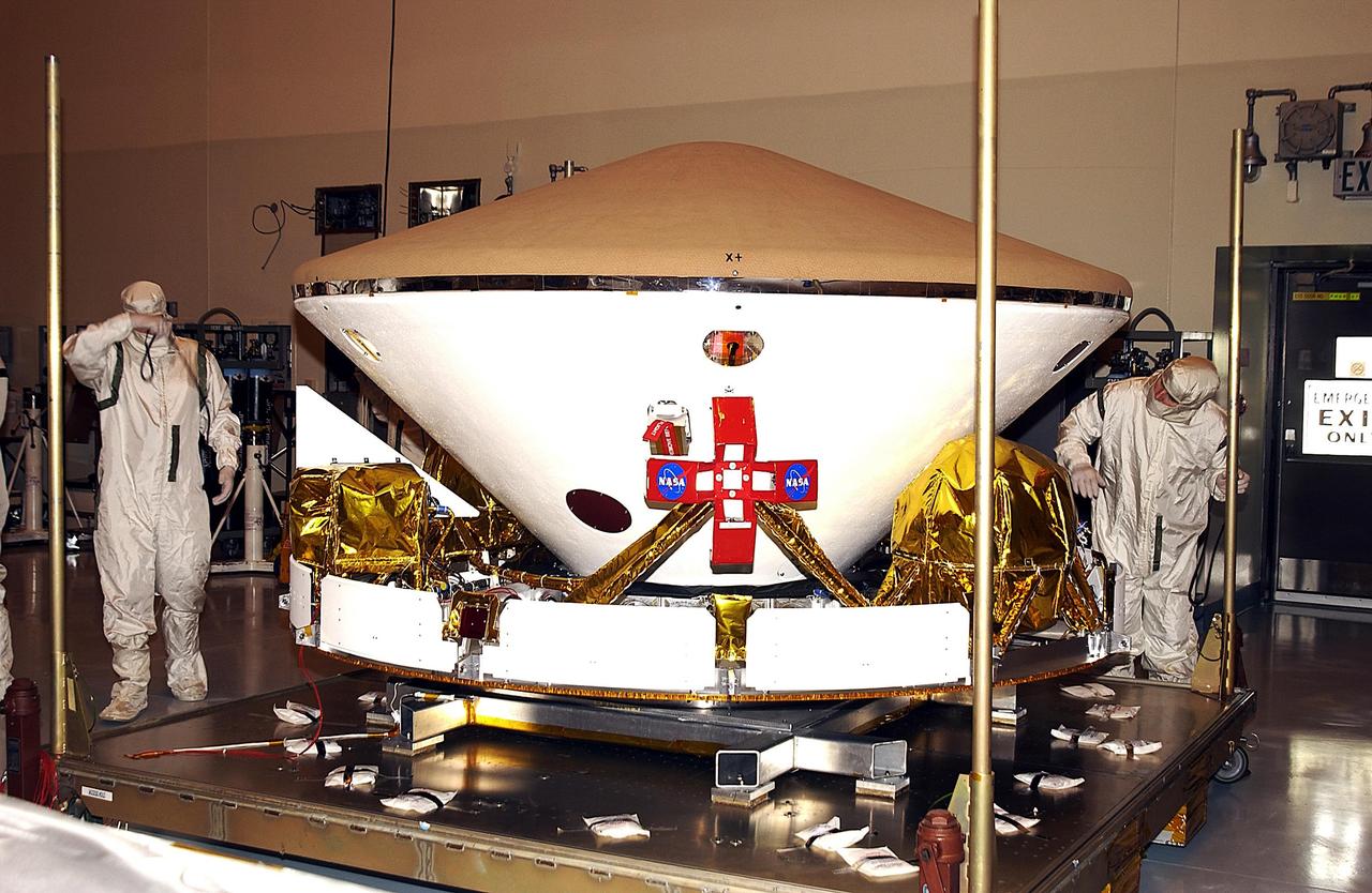 KENNEDY SPACE CENTER, FLA. - Workers in the Payload Hazardous Servicing Facility look over the aeroshell and cruise stage of Mars Exploration Rover-1. The upper portion is the heat shield on the aeroshell. Each rover , aeroshell and lander will undergo a full mission simulation while at KSC.  All flight elements will then be integrated.  After spin balance testing, each spacecraft will be mated to a solid propellant upper stage booster that will propel it out of Earth orbit.  The rovers will serve as robotic geologists to seek answers about the evolution of Mars, particularly  for a history of water. The rovers will be identical to each other, but will land at different regions of Mars.  Launch of the MER-1 is scheduled for May 30.  MER-2 will follow June 25.