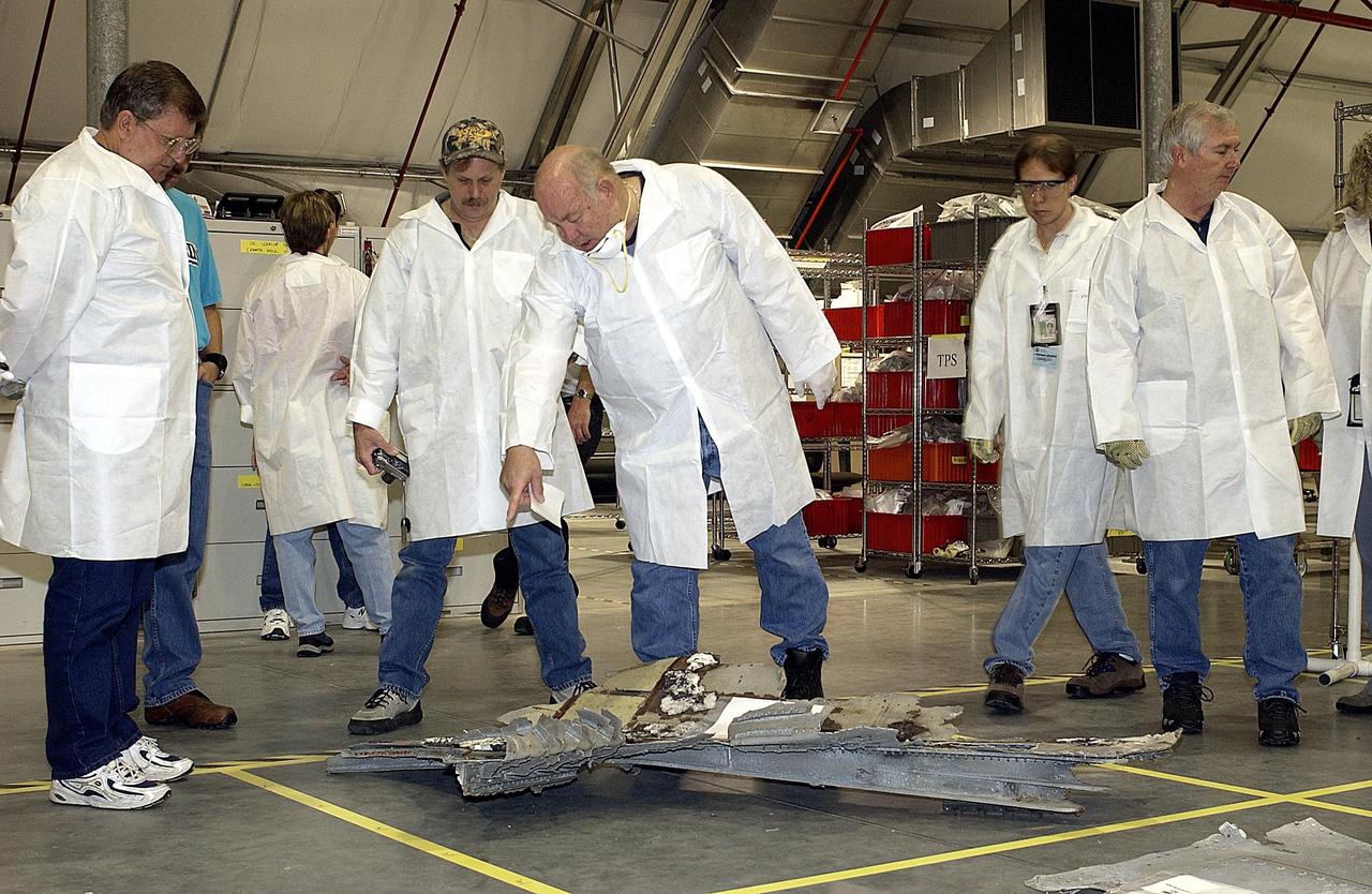 KENNEDY SPACE CENTER, FLA. -- Members of the Columbia Reconstruction Project Team look at a piece of Columbia debris placed on the floor grid of the RLV Hangar. The team will attempt to reconstruct the orbiter as part of the investigation into the accident that caused the destruction of Columbia and loss of its crew as it returned to Earth on mission STS-107.