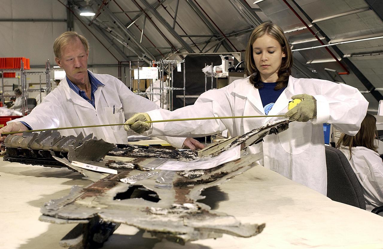 KENNEDY SPACE CENTER, FLA. - Two members of the Columbia Reconstruction Project Team measure a piece of Columbia debris collected and shipped from Barksdale Air Force Base, Shreveport, La. The Columbia Reconstruction Project Team is identifying pieces and placing them on the grid in a configuration of the orbiter. The team will attempt to reconstruct the orbiter as part of the investigation into the accident that caused the destruction of Columbia and loss of its crew as it returned to Earth on mission STS-107.