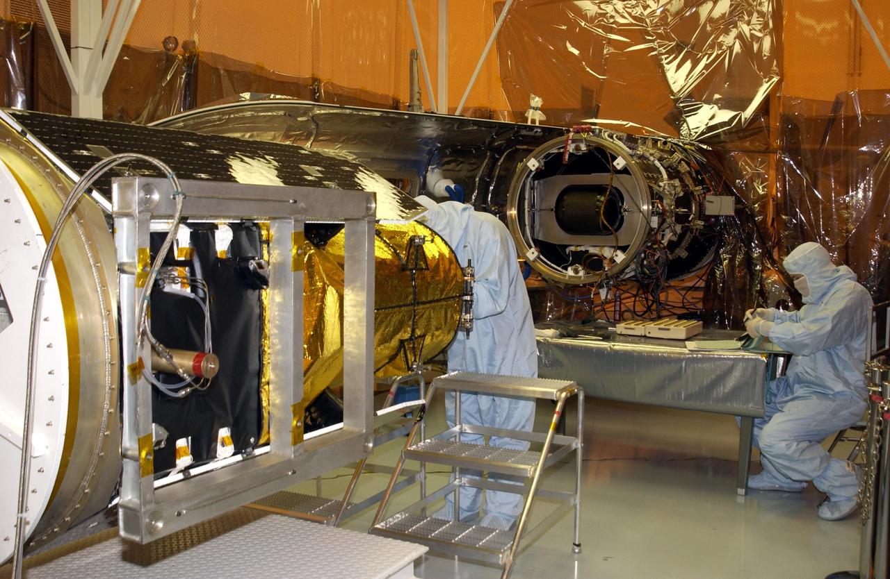 KENNEDY SPACE CENTER, FLA. -- A technician (left) works on NASA's Galaxy Evolution Explorer spacecraft after rotation.  The GALEX will be mated mating with the Pegasus XL launch vehicle. Set to launch April 2 from Cape Canaveral Air Force Station, the GALEX will carry into space an orbiting telescope that will observe a million galaxies across 10 billion years of cosmic history to help astronomers determine when the stars and elements we see today had their origins. From its orbit high above Earth, the spacecraft will sweep the skies for 28 months using state-of-the-art ultraviolet detectors.  Looking in the ultraviolet will single out galaxies dominated by young, hot, short-lived stars that give off a great deal of energy at that wavelength.  These galaxies are actively creating stars, and therefore provide a window into the history and causes of star formation in galaxies.