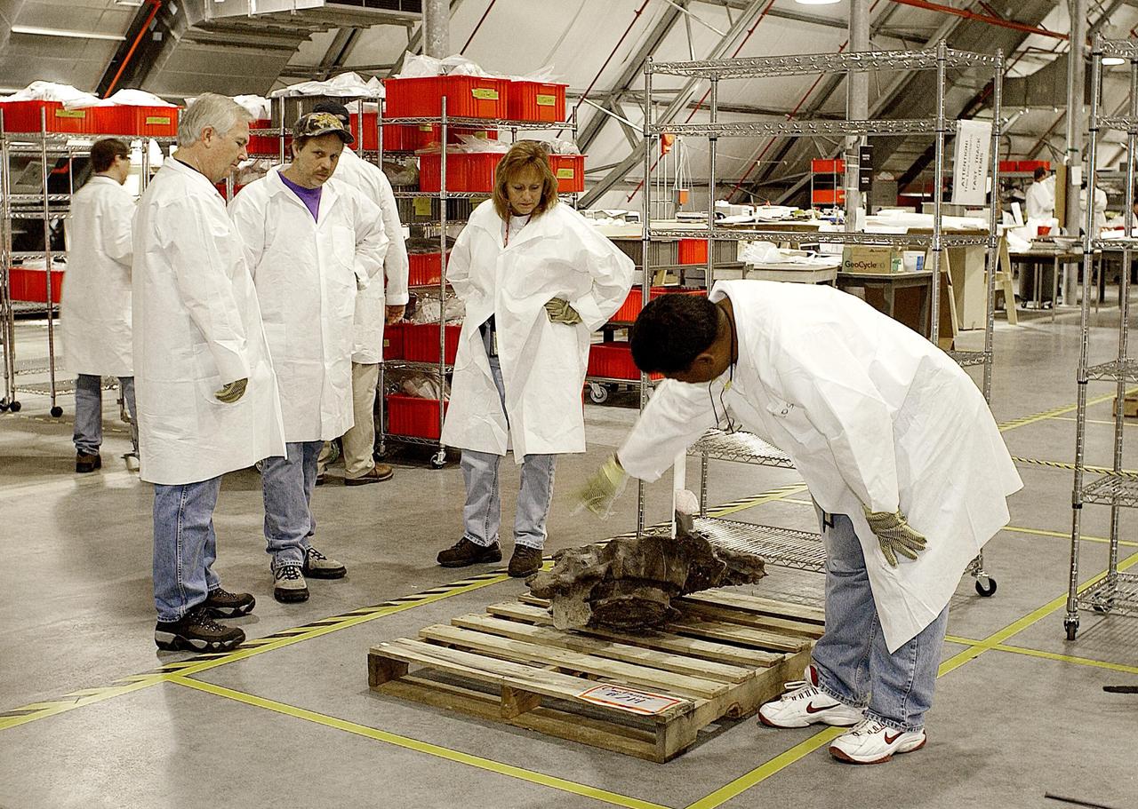 KENNEDY SPACE CENTER, FLA. - Members of the Columbia Reconstruction Project Team look at a piece of Columbia debris. The team is identifying pieces and placing them on a floor grid in a configuration of the orbiter. The team will attempt to reconstruct the orbiter as part of the investigation into the accident that caused the destruction of Columbia and loss of its crew as it returned to Earth on mission STS-107.