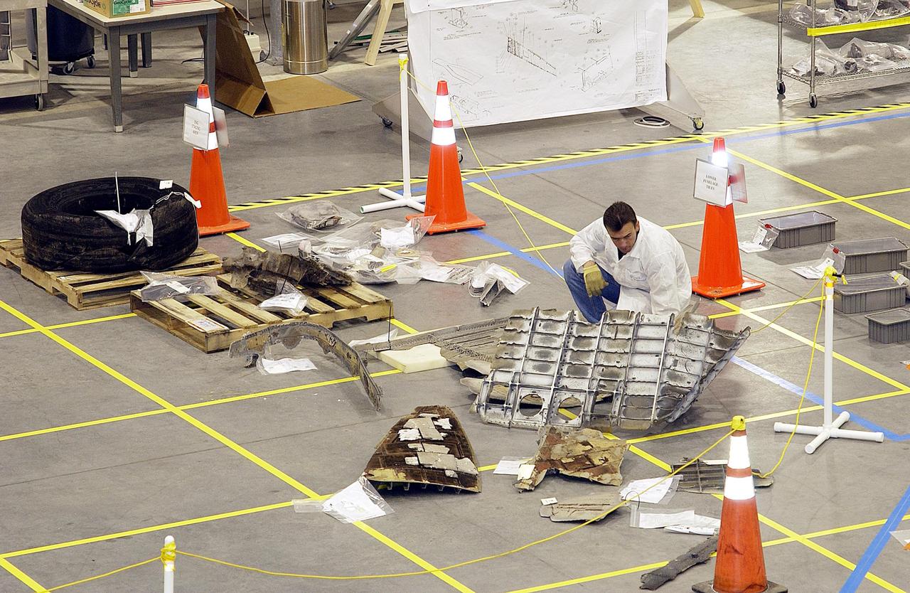 KENNEDY SPACE CENTER, FLA. - A member of the Columbia Reconstruction Project Team examines a piece of Columbia debris on the floor of the KSC RLV Hangar.  The team is attempting to identify the debris and reconstruct the orbiter as part of the investigation into the accident that caused the destruction of Columbia and loss of its crew as it returned to Earth on mission STS-107.