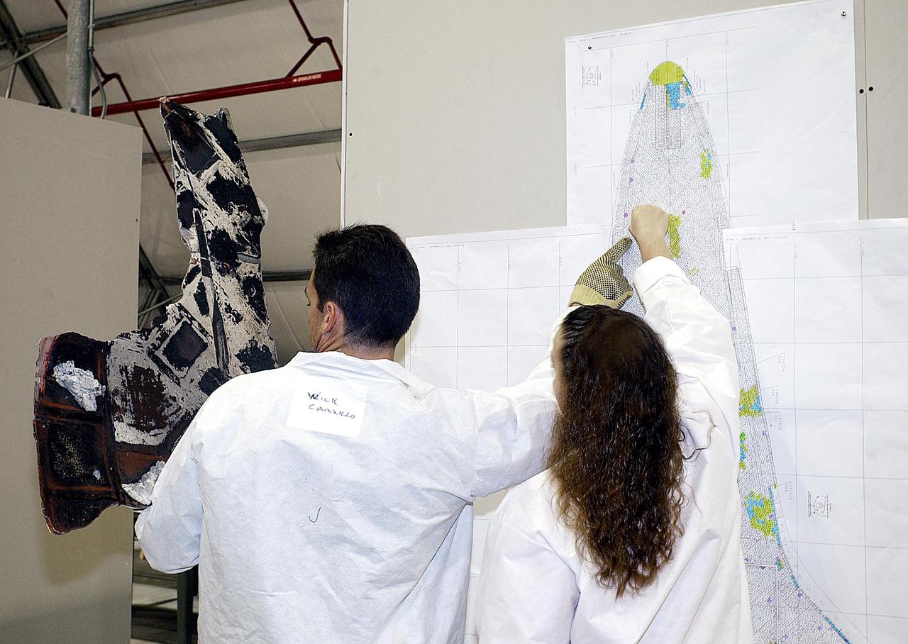 KENNEDY SPACE CENTER, FLA. -- - Two members of the Columbia Reconstruction Project Team examine a piece of Columbia debris, comparing it to a drawing of the orbiter. The team is attempting to identify the debris and reconstruct the orbiter as part of the investigation into the accident that caused the destruction of Columbia and loss of its crew as it returned to Earth on mission STS-107.