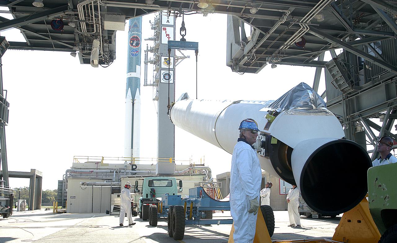 One of nine solid rocket boosters is lifted on Launch Complex 17-B, Cape Canaveral Air Force Station, for mating with the Delta II rocket in the background. The second stage will later be hoisted atop the first stage. The Delta rocket is the launch vehicle for the Space Infrared Telescope Facility. SIRTF will obtain images and spectra by detecting the infrared energy, or heat, radiated by objects in space. Most of this infrared radiation is blocked by the Earth's atmosphere and cannot be observed from the ground. Consisting of an 0.85-meter telescope and three cryogenically cooled science instruments, SIRTF is one of NASA's largest infrared telescopes to be launched. SIRTF is scheduled for launch April 15 at 4:34:07 a.m. EDT.