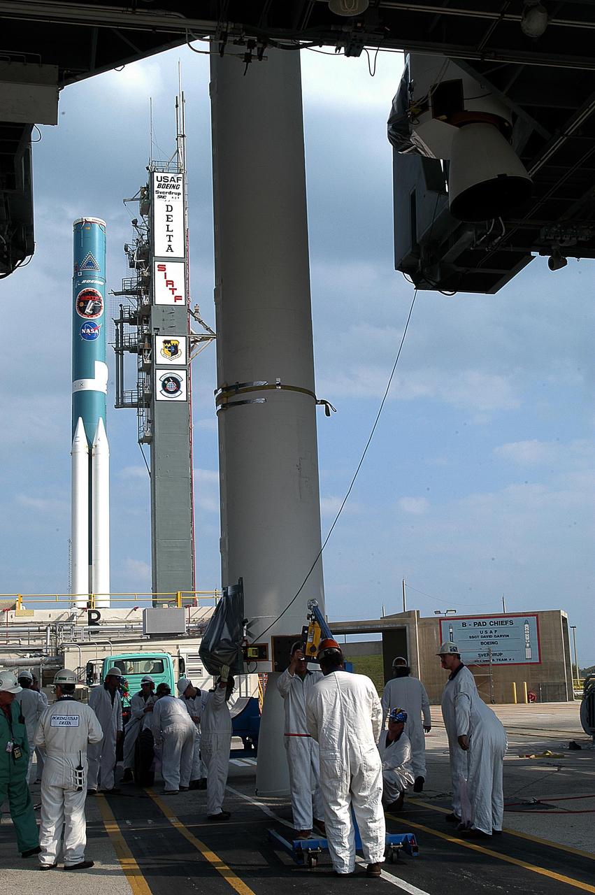 KENNEDY SPACE CENTER, FLA. - Workers maneuver another solid rocket booster that will be mated with the Delta II rocket in the background. The Delta II will launch the Space Infrared Telescope Facility. The second stage will later be hoisted atop the first stage.  SIRTF will obtain images and spectra by detecting the infrared energy, or heat, radiated by objects in space. Most of this infrared radiation is blocked by the Earth's atmosphere and cannot be observed from the ground. Consisting of an 0.85-meter telescope and three cryogenically cooled science instruments, SIRTF is one of NASA's largest infrared telescopes to be launched.