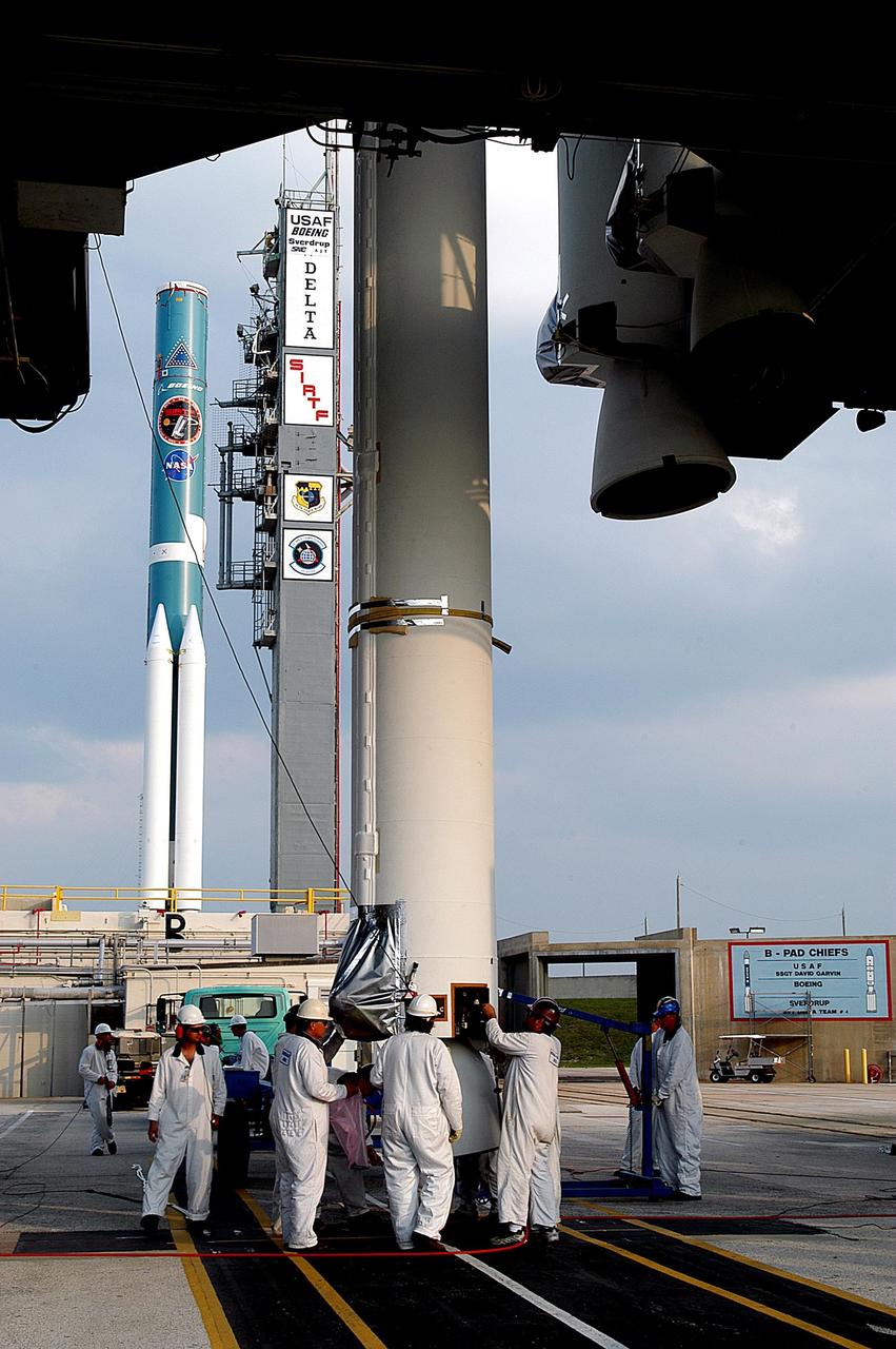 KENNEDY SPACE CENTER, FLA. - On Launch Complex 17-B, Cape Canaveral Air Force Station, workers prepare another solid rocket booster that will be mated with the Delta II rocket in the background. The Delta II will launch the Space Infrared Telescope Facility. The second stage will later be hoisted atop the first stage.  SIRTF will obtain images and spectra by detecting the infrared energy, or heat, radiated by objects in space. Most of this infrared radiation is blocked by the Earth's atmosphere and cannot be observed from the ground. Consisting of an 0.85-meter telescope and three cryogenically cooled science instruments, SIRTF is one of NASA's largest infrared telescopes to be launched.