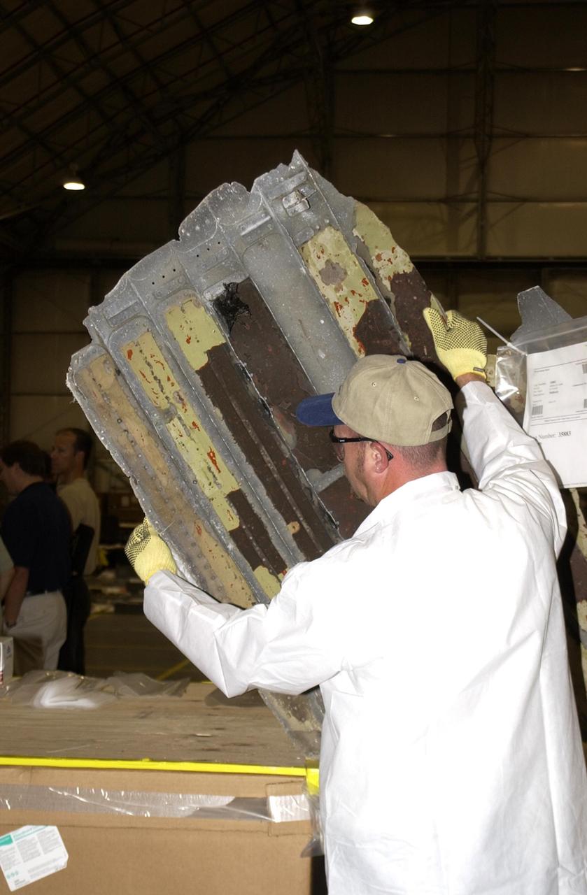 KENNEDY SPACE CENTER, Fla. - A member of the Columbia Reconstruction Project Team looks at piece of Columbia debris newly arrived from Barksdale Air Force Base, Shreveport, La. Inside the RLV Hangar, the team is identifying pieces and placing them on a floor grid in a configuration of the orbiter. The team will attempt to reconstruct the bottom of the orbiter as part of the investigation into the accident that caused the destruction of Columbia and loss of its crew as it returned to Earth on mission STS-107. To date, 35,319 pieces have been shipped to KSC; 1,218 are identified and placed on the grid.