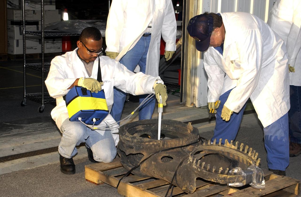 KENNEDY SPACE CENTER, Fla. - Members of the Columbia Reconstruction Project Team check out a piece of Columbia debris newly arrived from Barksdale Air Force Base, Shreveport, La. Inside the RLV Hangar, the team is identifying pieces and placing them on a floor grid in a configuration of the orbiter. The team will attempt to reconstruct the bottom of the orbiter as part of the investigation into the accident that caused the destruction of Columbia and loss of its crew as it returned to Earth on mission STS-107. To date, 35,319 pieces have been shipped to KSC; 1,218 are identified and placed on the grid.