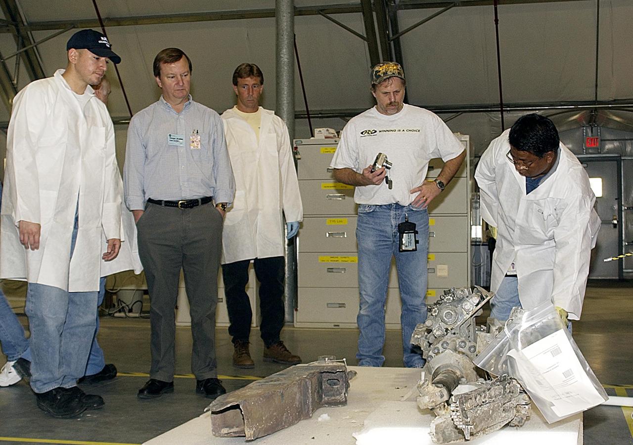 KENNEDY SPACE CENTER, Fla. - In the RLV Hangar, members of the Columbia Reconstruction Project Team look at a piece of debris.  Second from left is Mike Leinbach, who is Shuttle launch director.  To date, 35,319 pieces of debris have been shipped to KSC; 1,218 have been identified and placed on a grid in a configuration of the orbiter.  The team is attempting to reconstruct the bottom of the orbiter as part of the investigation into the accident that caused the destruction of Columbia and loss of its crew as it returned to Earth on mission STS-107.