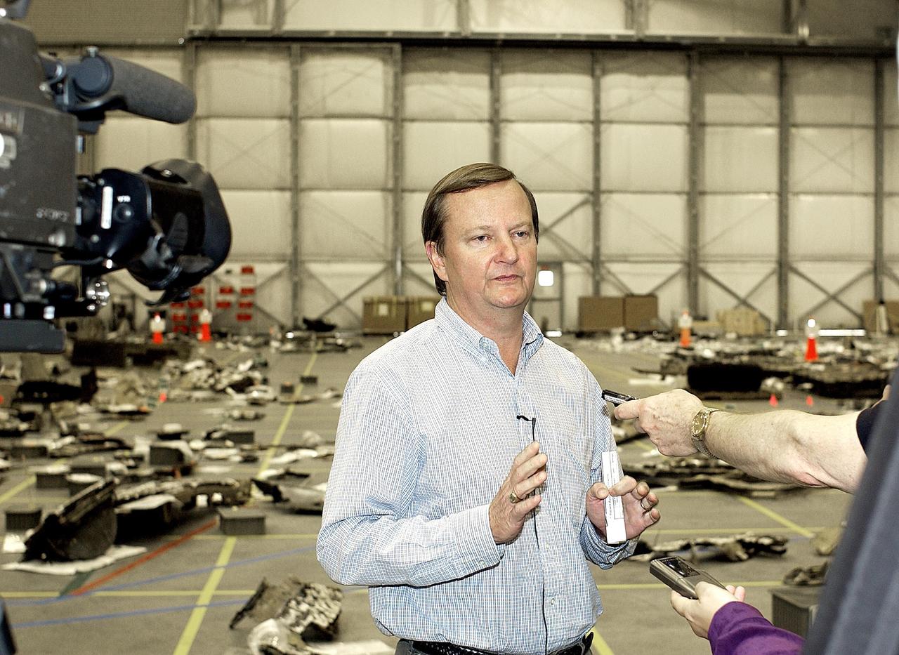 KENNEDY SPACE CENTER, FLA. -  Shuttle Launch Director Mike Leinbach answers reporters' questions in the RLV Hangar.   Leinbach is overseeing assessment of the debris, seen in the background, as it is delivered to KSC.  The Columbia Reconstruction Project team is identifying pieces and placing them on a grid approximating the shape of the orbiter.  About 25 percent of the orbiter has been delivered to the hangar.