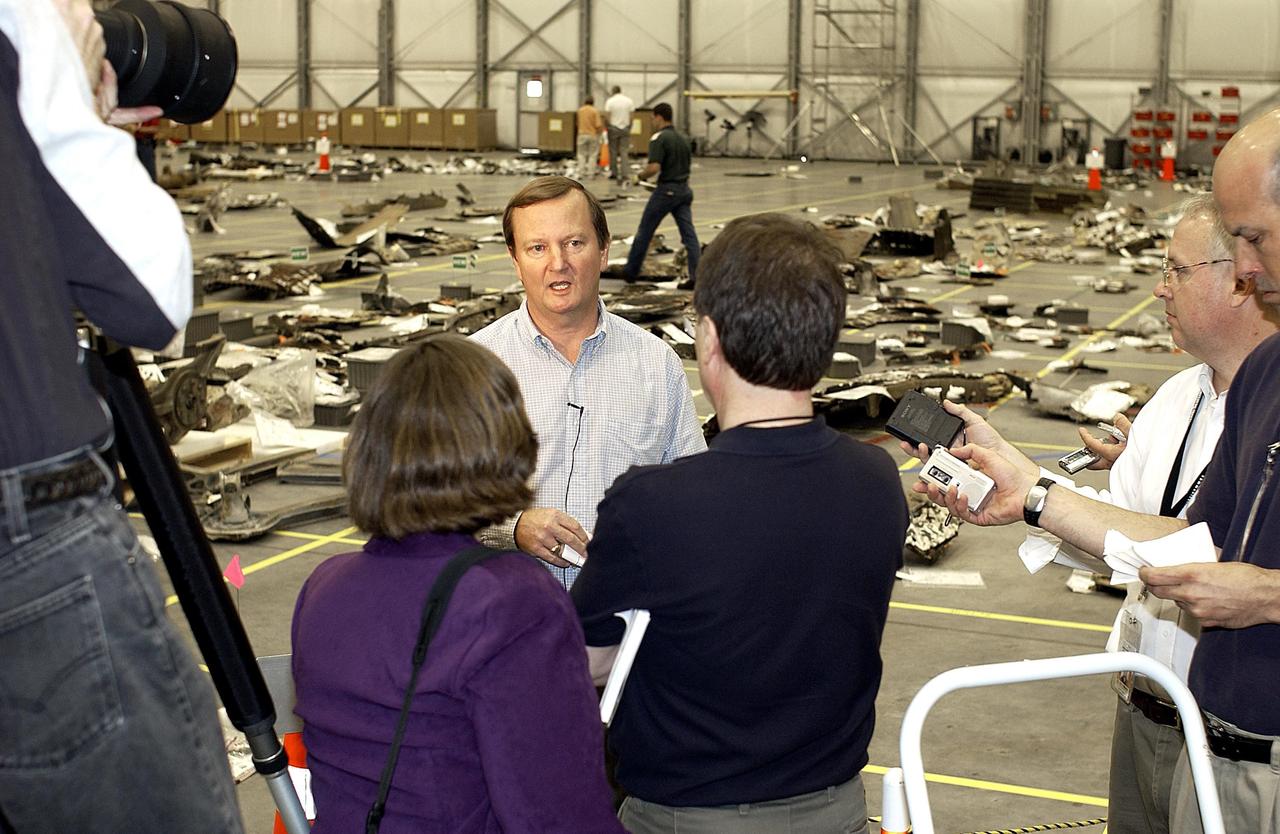 KENNEDY SPACE CENTER, FLA. -  Shuttle Launch Director Mike Leinbach answers reporters' questions in the RLV Hangar.   Leinbach is overseeing assessment of the debris, seen in the background, as it is delivered to KSC.  The Columbia Reconstruction Project team is identifying pieces and placing them on a grid approximating the shape of the orbiter.  About 25 percent of the orbiter has been delivered to the hangar.