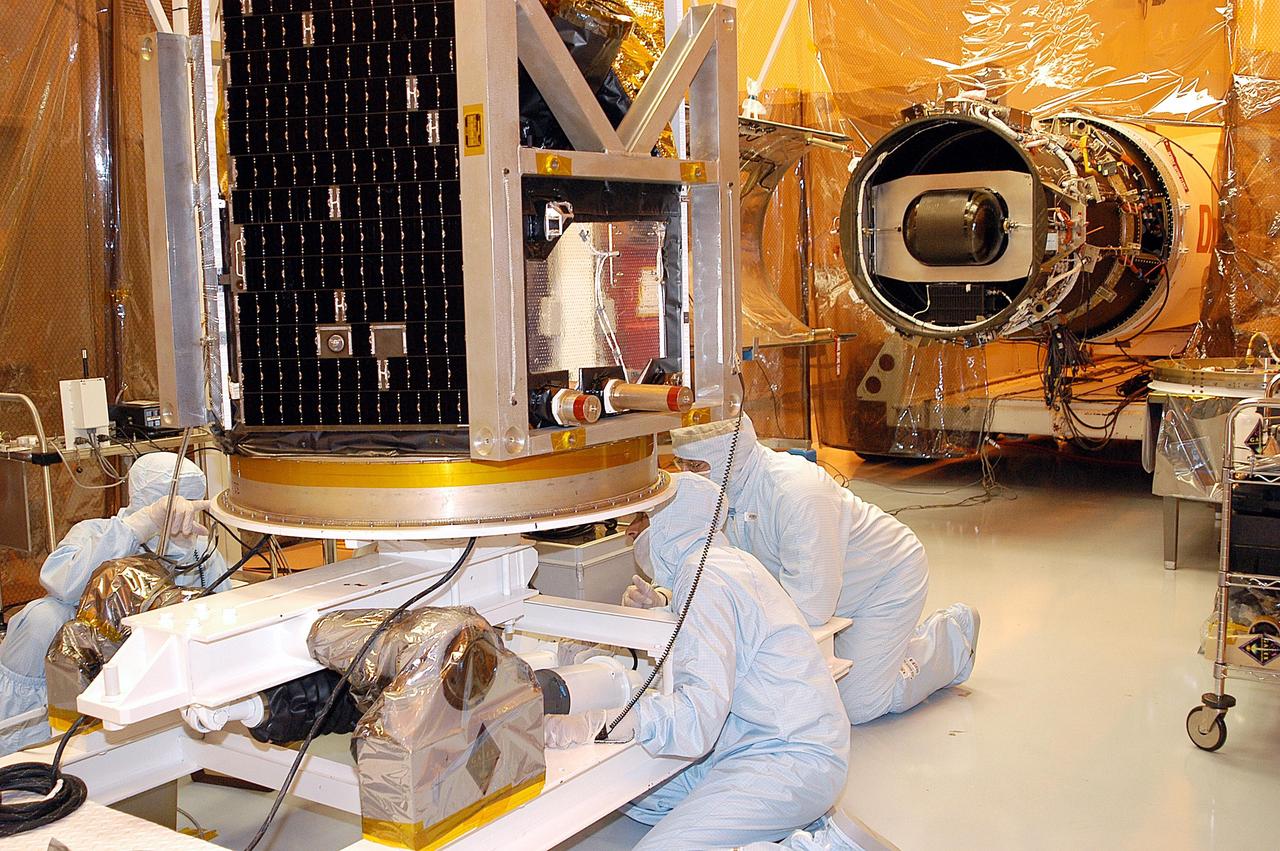 KENNEDY SPACE CENTER, FLA. -  Technicians verify that the Galaxy Evolution Explorer (GALEX) spacecraft is secure on its workstand after being moved into a vertical position in the Payload Hazardous Servicing Facility.  On the right is the Pegasus launch vehicle from which it was demated. A borescope inspection will be conducted on the spacecraft to locate a small fastener and associated clip missing from a demated connector identified during preflight testing. GALEX is an orbiting space telescope that will observe galaxies in ultraviolet light across 10 billion years of cosmic history. During its 29-month mission, GALEX will produce the first comprehensive map of a Universe of galaxies under construction, bringing more understanding to how galaxies like the Milky Way were formed. The GALEX launch date in late April is currently under review.