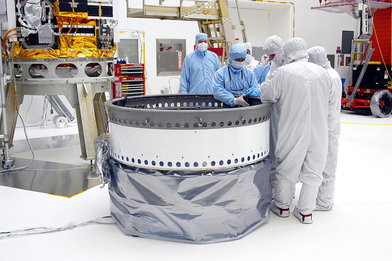 KENNEDY SPACE CENTER, FLA. -- Workers in Building AE adjust the payload attach fitting for the Space Infrared Telescope Facility (SIRTF), in the background. SIRTF will be mated with the Delta II launch vehicle via the fitting. SIRTF is currently scheduled for transportation to Launch Complex 17-B, Cape Canaveral Air Force Station, and hoisting atop the Delta II on or about April 4.