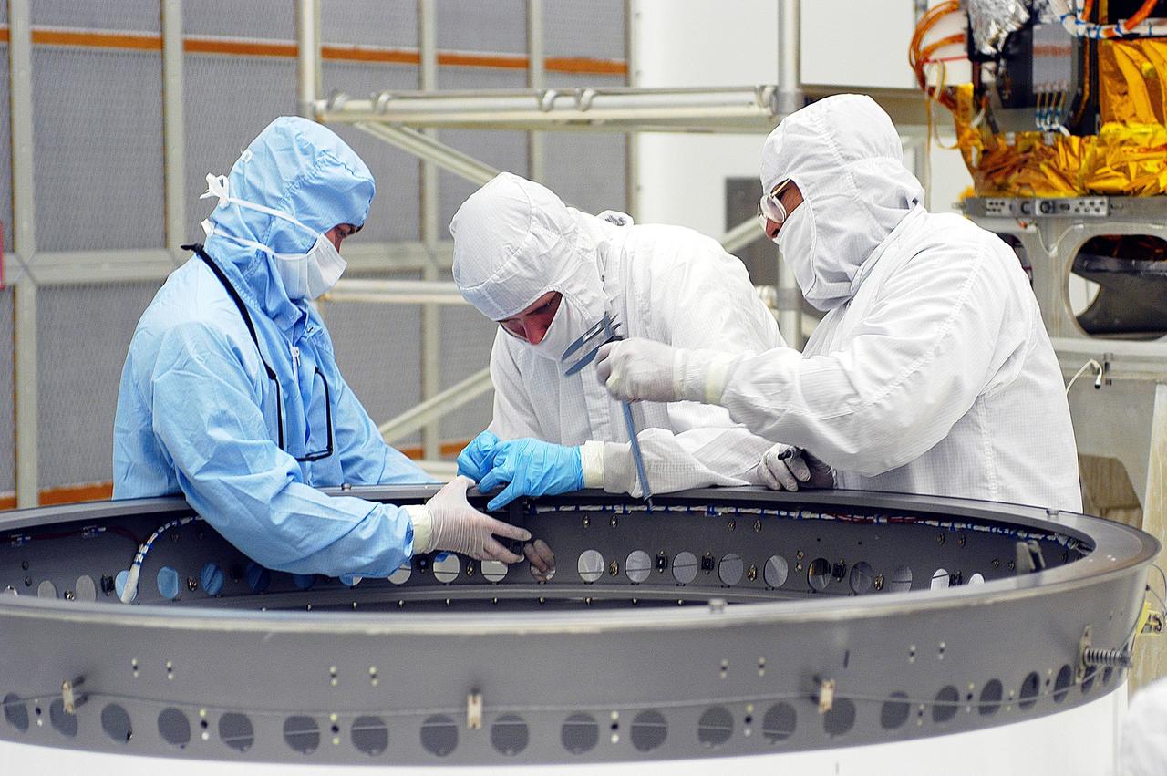 KENNEDY SPACE CENTER, FLA. - Workers in Building AE adjust the payload attach fitting for the Space Infrared Telescope Facility (SIRTF). SIRTF will be mated with the Delta II launch vehicle via the fitting. SIRTF is currently scheduled for transportation to Launch Complex 17-B, Cape Canaveral Air Force Station, and hoisting atop the Delta II on or about April 4.