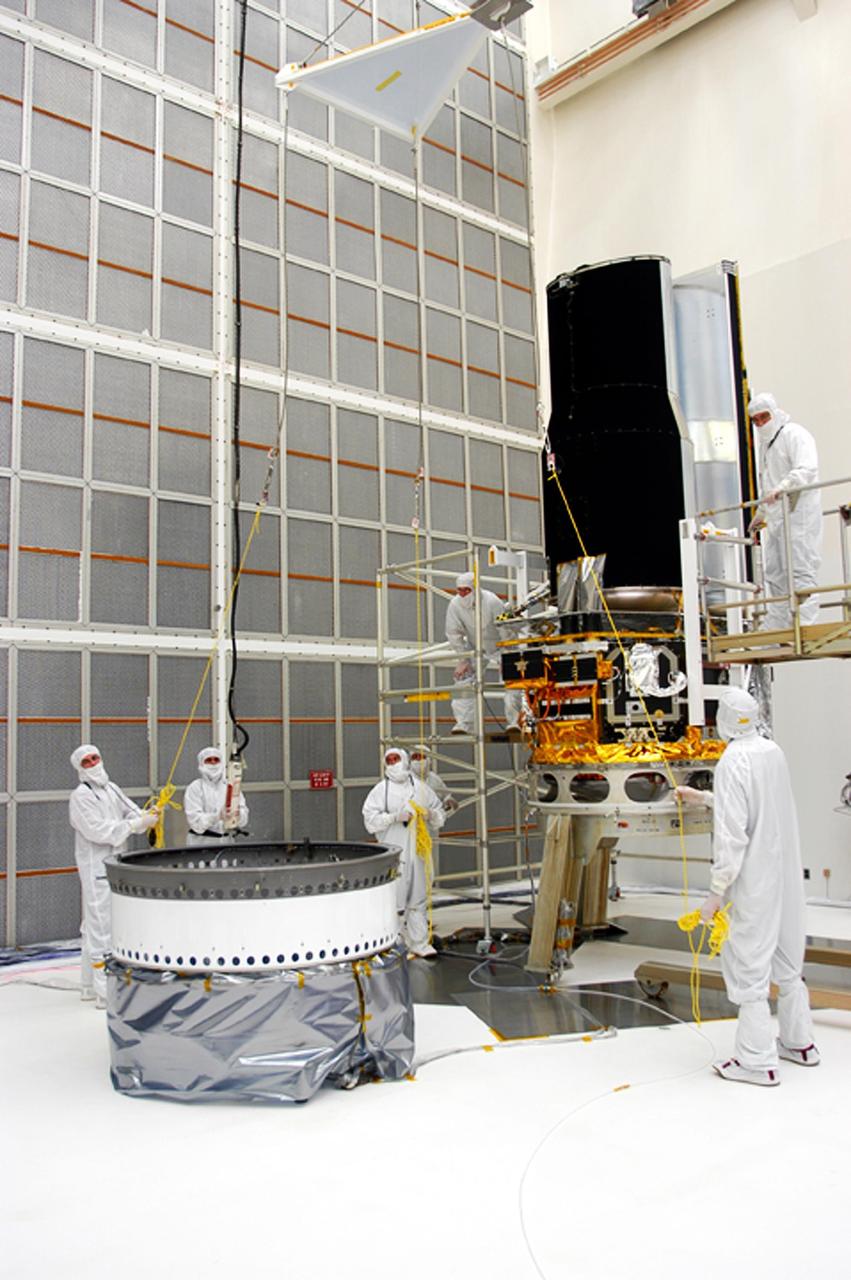 KENNEDY SPACE CENTER, FLA. - Workers in Building AE lower a part of the protective covering for the Space Infrared Telescope Facility (SIRTF), seen at right. SIRTF will be mated with its Delta II launch vehicle via the fitting seen at left. SIRTF is currently scheduled for transportation to Launch Complex 17-B, Cape Canaveral Air Force Station, and hoisting atop the Delta II on or about April 4.