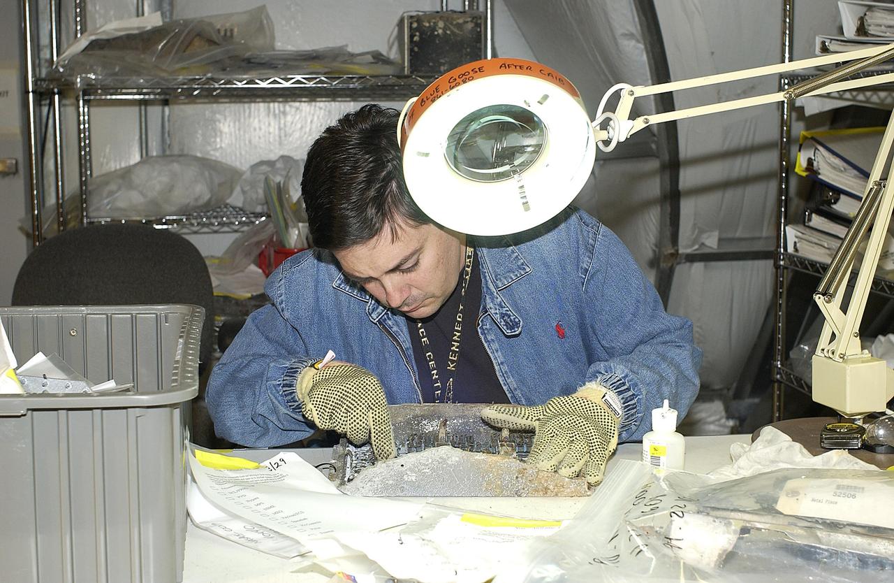 KENNEDY SPACE CENTER, FLA. -  A member of the Columbia Reconstruction Project Team examines a piece of Columbia debris in the RLV Hangar.  Approximately 4,500 ground searchers have covered approximately 56 percent of the planned 555,000-acre search area. About 28 percent of the Shuttle Columbia, by weight, has been delivered to the RLV Hangar to date.