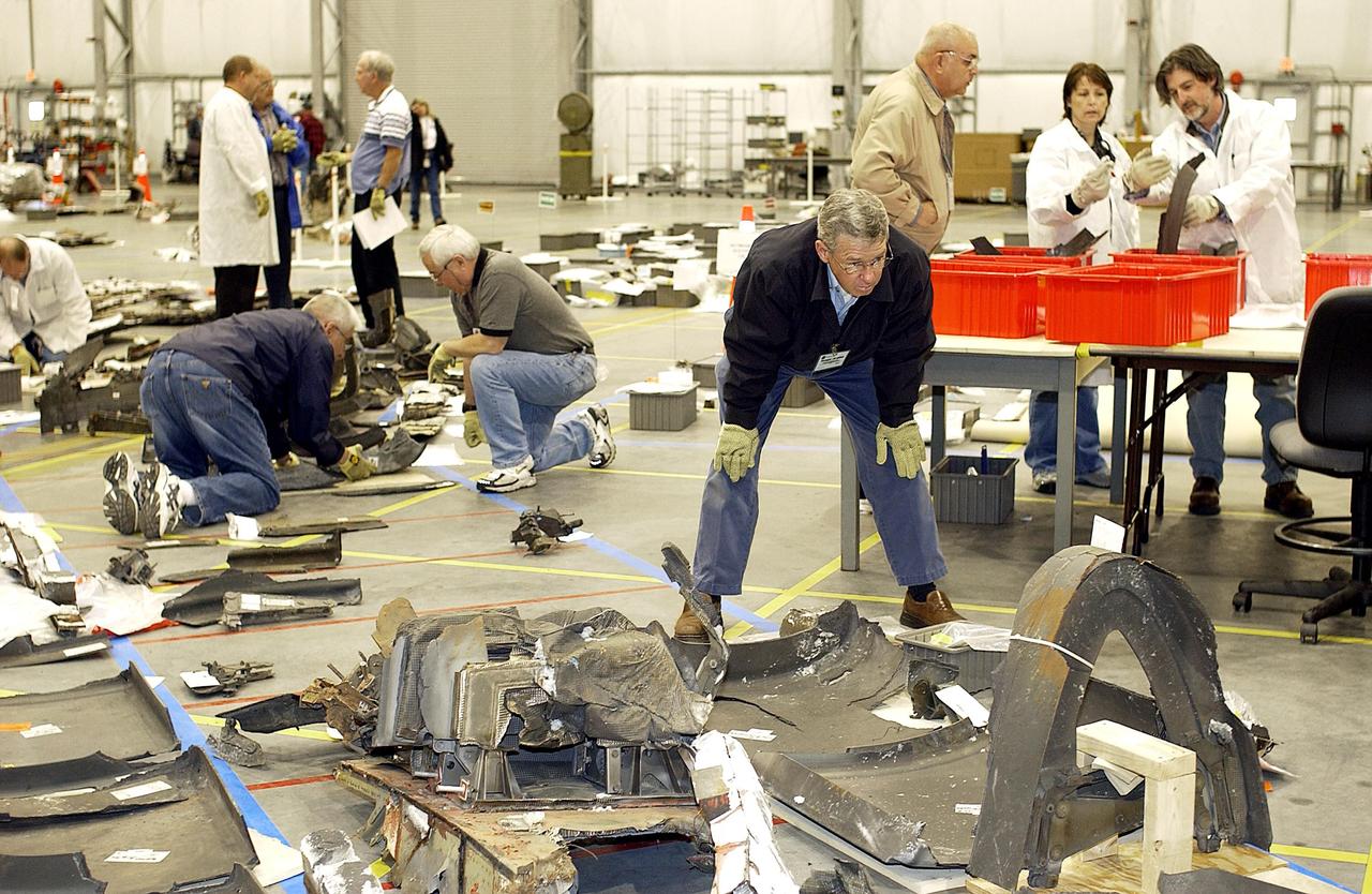 KENNEDY SPACE CENTER, FLA. -  Members of the Columbia Reconstruction Project Team look over various pieces of Columbia debris spread across the floor of the RLV Hangar.  Approximately 4,500 ground searchers have covered approximately 56 percent of the planned 555,000-acre search area. About 28 percent of the Shuttle Columbia, by weight, has been delivered to the RLV Hangar to date.