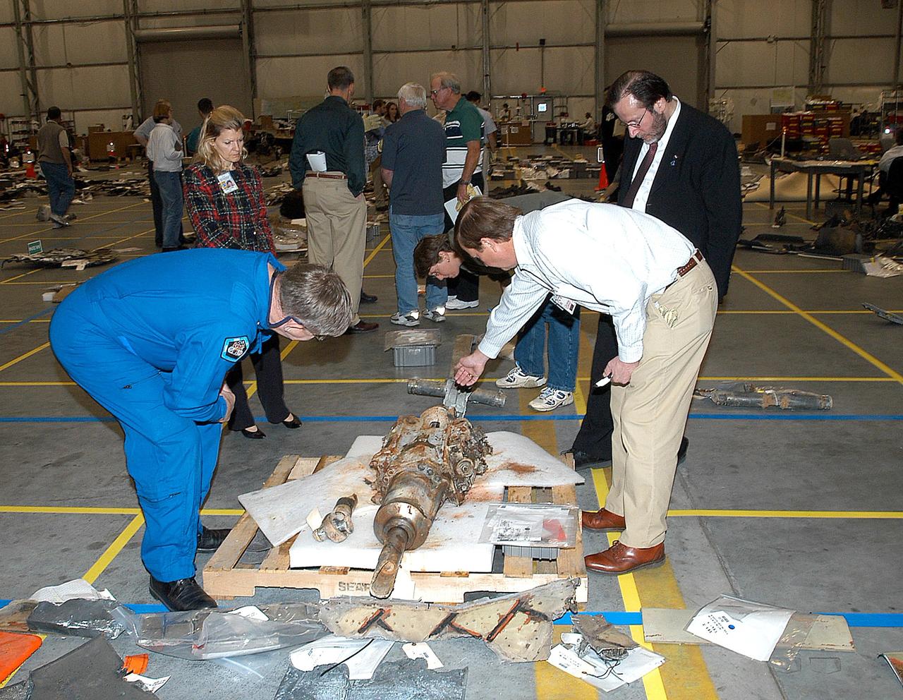 KENNEDY SPACE CENTER, FLA. -  -  In the RLV Hangar at KSC, examining a piece of debris from Space Shuttle Columbia are former payload specialist Dr. Roger Crouch (left), Shuttle Launch Director Mike Leinbach (right, pointing) and NASA Chief of Staff and White House liaison Courtney Stadd (right).  The debris is one of more than 35,000 pieces collected so far.  More than 1,218 pieces have been identified. The search of more than 500,000 acres of primary recovery area for Columbia material has passed the halfway mark.  To date about 28 percent of Columbia, by weight, has been delivered to the hangar.