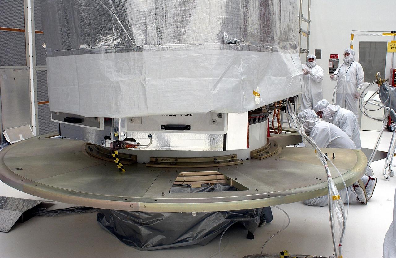 KENNEDY SPACE CENTER, FLA. - The Space Infrared Telescope Facility is shrouded while workers install the base plate segments for the canister. SIRTF will obtain images and spectra by detecting the infrared energy, or heat, radiated by objects in space. Most of this infrared radiation is blocked by the Earth's atmosphere and cannot be observed from the ground. Consisting of an 0.85-meter telescope and three cryogenically cooled science instruments, SIRTF is one of NASA's largest infrared telescopes to be launched. SIRTF is currently scheduled for launch aboard a Delta II rocket from Launch Complex 17-B, Cape Canaveral Air Force Station.