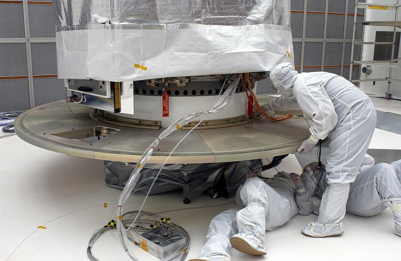 KENNEDY SPACE CENTER, FLA. - Workers add another base plate segment to the shrouded Space Infrared Telescope Facility. The base plate is being added for the canister. SIRTF will obtain images and spectra by detecting the infrared energy, or heat, radiated by objects in space. Most of this infrared radiation is blocked by the Earth's atmosphere and cannot be observed from the ground. Consisting of an 0.85-meter telescope and three cryogenically cooled science instruments, SIRTF is one of NASA's largest infrared telescopes to be launched. SIRTF is currently scheduled for launch aboard a Delta II rocket from Launch Complex 17-B, Cape Canaveral Air Force Station.