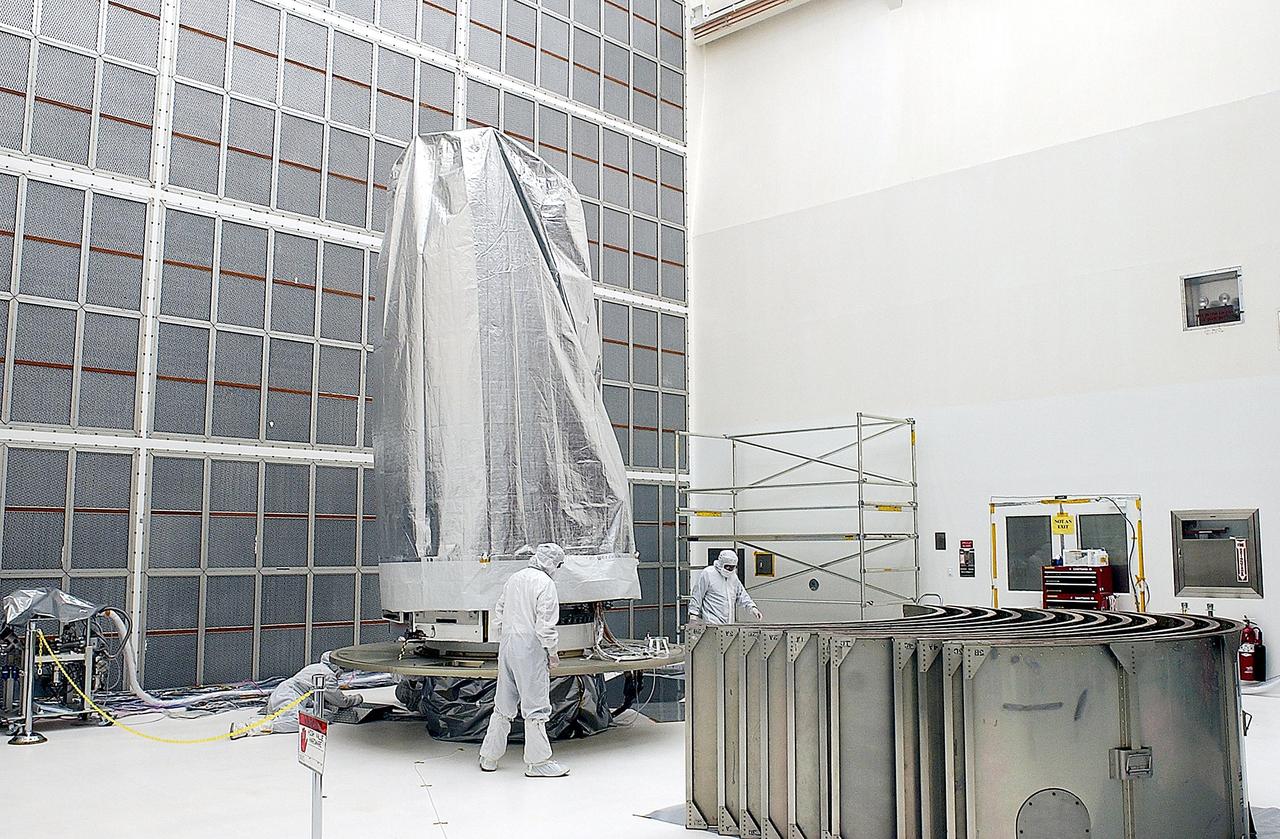 KENNEDY SPACE CENTER, FLA. - Workers in Building AE prepare the Space Infrared Telescope Facility (SIRTF), in the background, for buildup of the payload canister. SIRTF will be mated with the Delta II launch vehicle via the payload attach fitting at the bottom. SIRTF is currently scheduled for transportation to Launch Complex 17-B, Cape Canaveral Air Force Station, and hoisting atop the Delta II on or about April 4.