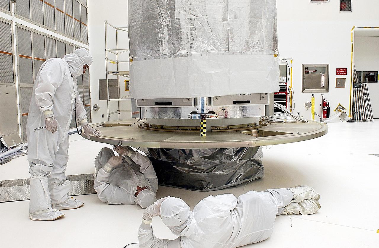 KENNEDY SPACE CENTER, FLA. -- Workers in Building AE adjust the payload attach fitting on the Space Infrared Telescope Facility (SIRTF) before buildup of the payload canister. SIRTF will be mated with the Delta II launch vehicle via the fitting. SIRTF is currently scheduled for transportation to Launch Complex 17-B, Cape Canaveral Air Force Station, and hoisting atop the Delta II on or about April 4.