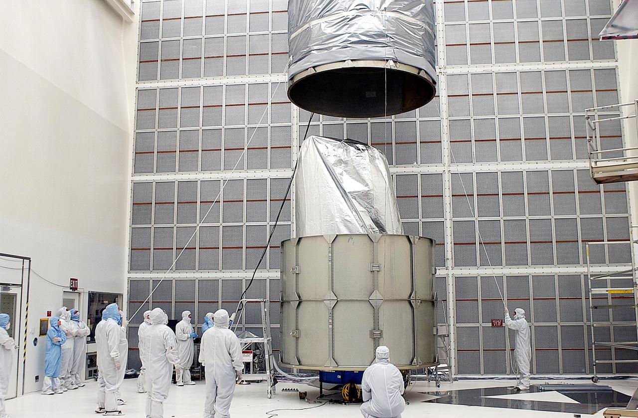 KENNEDY SPACE CENTER, FLA. - Workers guide the movement of the top rings of the payload canister over the Space Infrared Telescope Facility (SIRTF) below. After installation, SIRTF will be transported to Launch Complex 17-B, Cape Canaveral Air Force Station, and mating with the Delta II on or about April 4.
