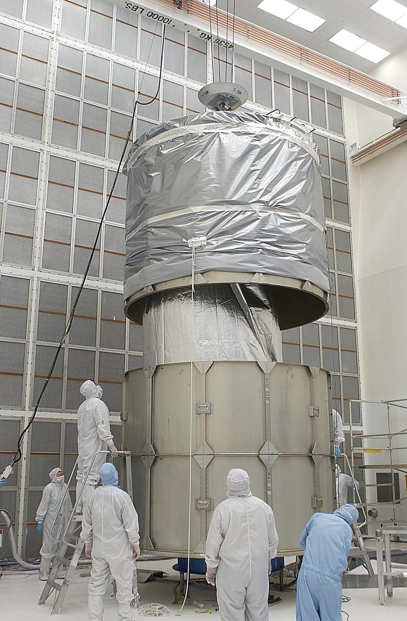 KENNEDY SPACE CENTER, FLA. -- Workers lower the top rings of the payload canister over the Space Infrared Telescope Facility (SIRTF) below. After installation, SIRTF will be transported to Launch Complex 17-B, Cape Canaveral Air Force Station, and mating with the Delta II on or about April 4.
