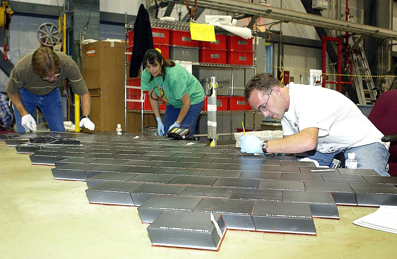 KENNEDY SPACE CENTER, FLA. -- In the Orbiter Processing Facility, United Space Alliance employees (from left) Harrell Watts, Lynn Wozniak, and Jason Levandusky install Thermal Protection System tiles on a main landing gear door of Space Shuttle orbiter Enterprise (OV-101).  Sections of Enterprise were borrowed from the Smithsonian Institution's Air and Space Museum where the orbiter is being stored at the Washington Dulles International Airport.  Enterprise was the first orbiter built in the Shuttle fleet and was used to conduct the Approach and Landing Test Program before the first powered Shuttle flight.  After the tile installation is complete, the sections will be transferred to the Southwest Research Institute for testing requested by the Columbia Accident Investigation Board.