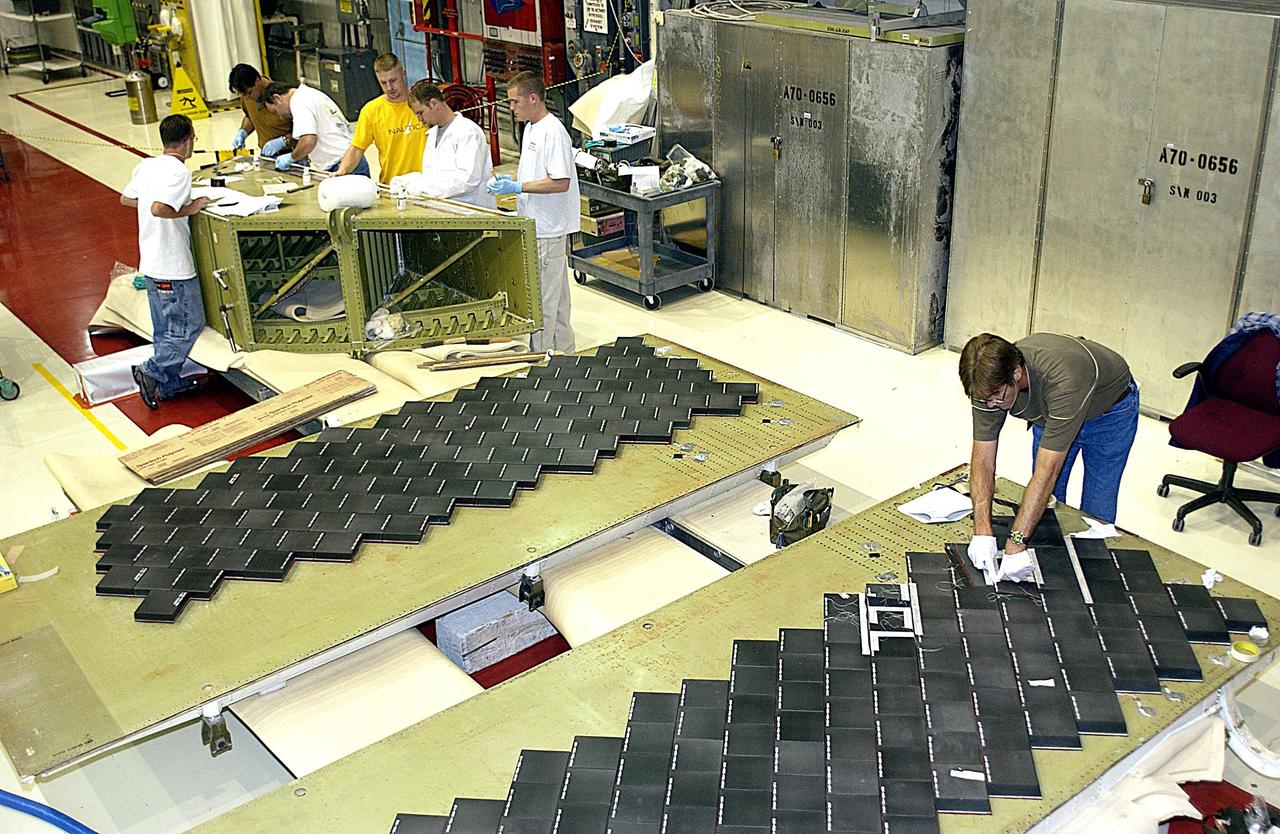 KENNEDY SPACE CENTER, FLA. -- In the Orbiter Processing Facility (OPF), United Space Alliance (USA) employee Harrell Watts (right) installs Thermal Protection System (TPS) tiles on a main landing gear door of Space Shuttle orbiter Enterprise (OV-101).  In the background, other USA employees, members of the OPF midbody TPS crew, prepare to install TPS tile on a simulated orbiter wing.  The wing and the sections of Enterprise will be transferred to the Southwest Research Institute for testing after the tile installation is complete. The testing has been requested by the Columbia Accident Investigation Board. Sections of Enterprise were borrowed from the Smithsonian Institution's Air and Space Museum where the orbiter is being stored at the Washington Dulles International Airport. Enterprise was the first orbiter built in the Shuttle fleet and was used to conduct the Approach and Landing Test Program before the first powered Shuttle flight.